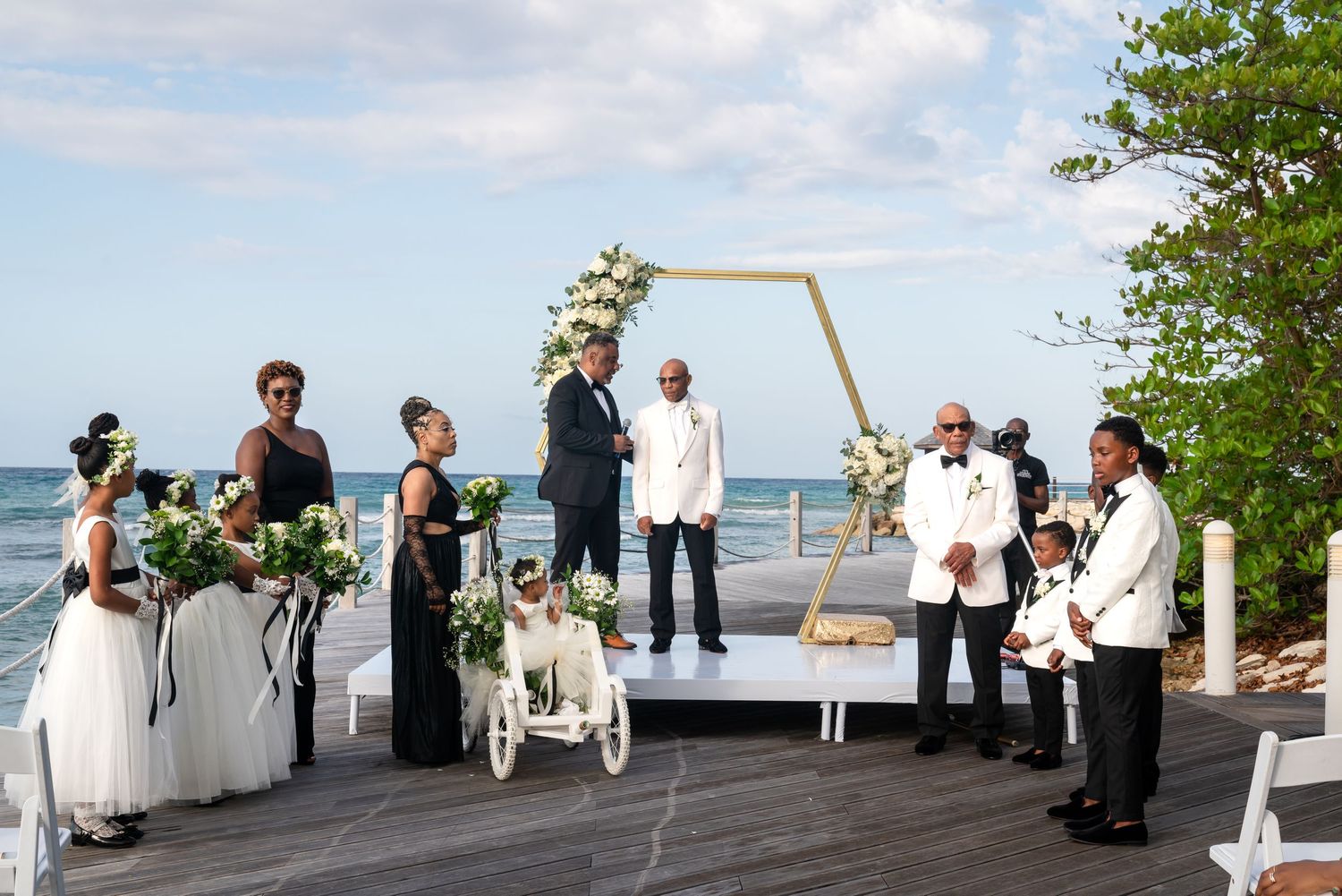 Wedding attendees gather on a beach deck overlooking the water during an outdoor ceremony.