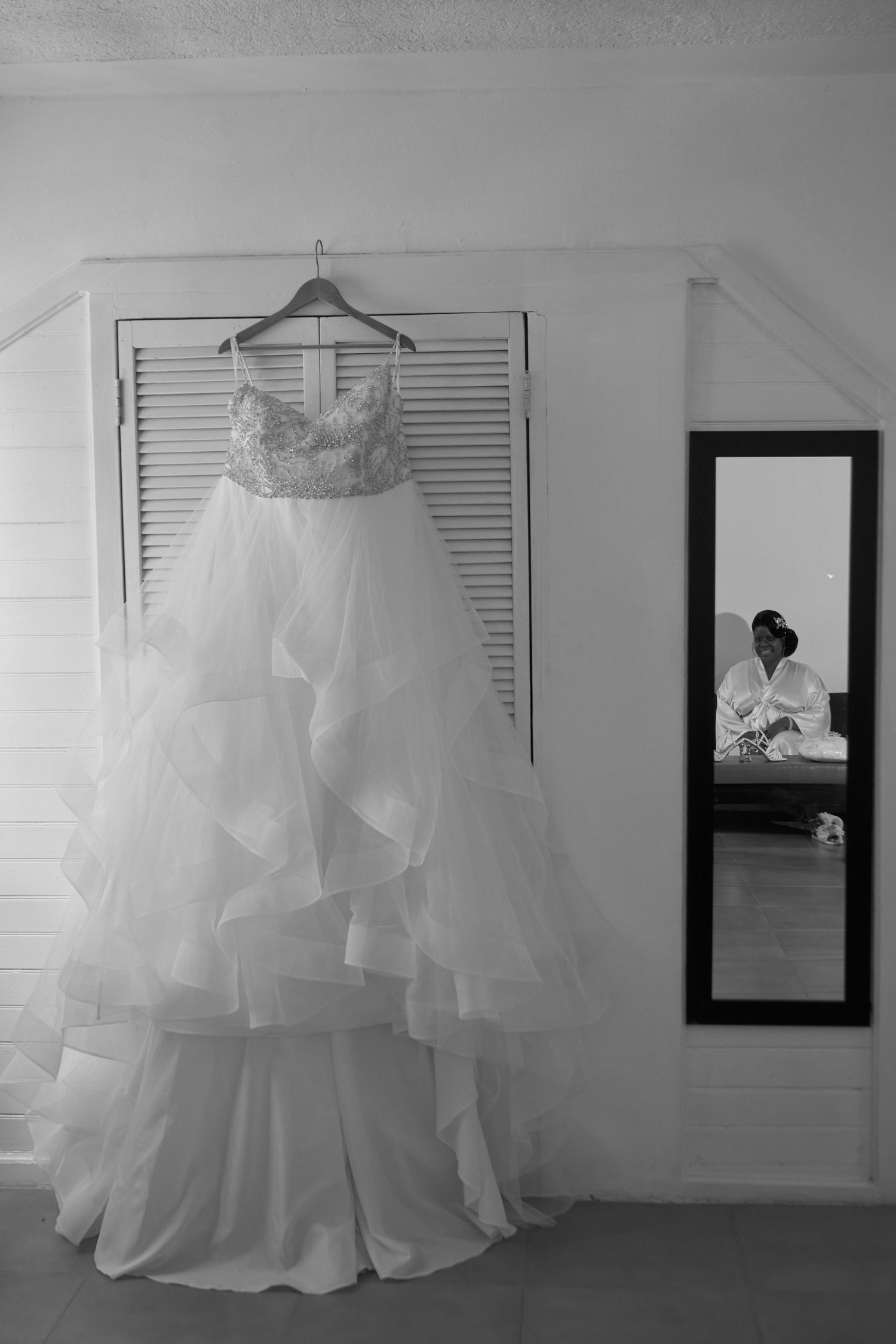 A series of black and white wedding dress photos showing the gown hanging elegantly against white shutters and walls.