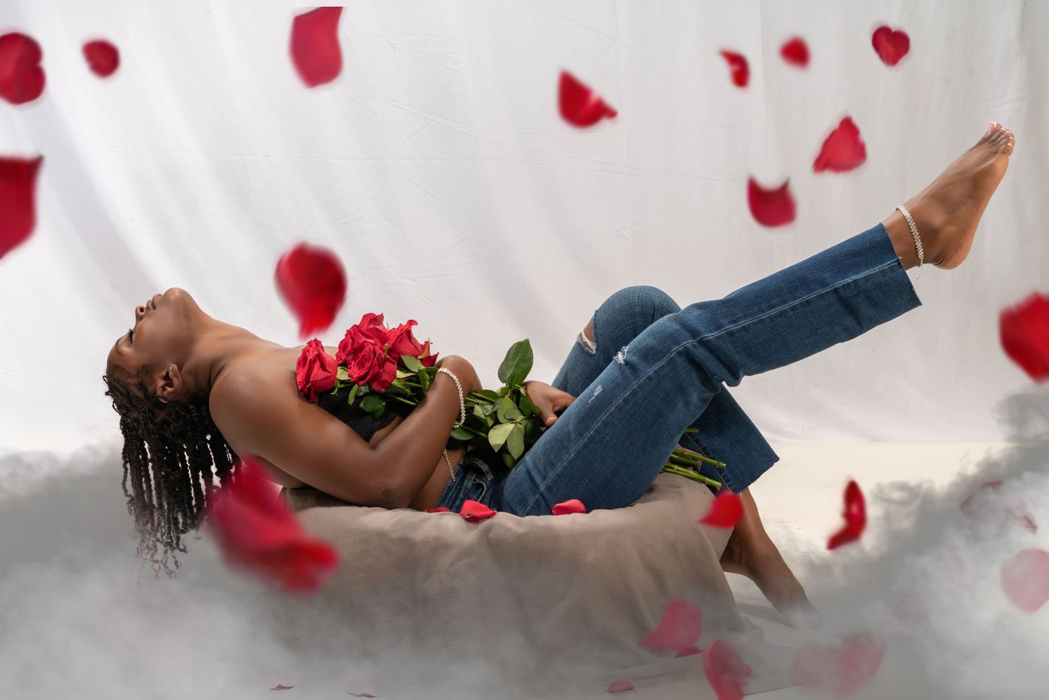 Rose petals falling against a white background as a young woman holds a bouquet of flowers.