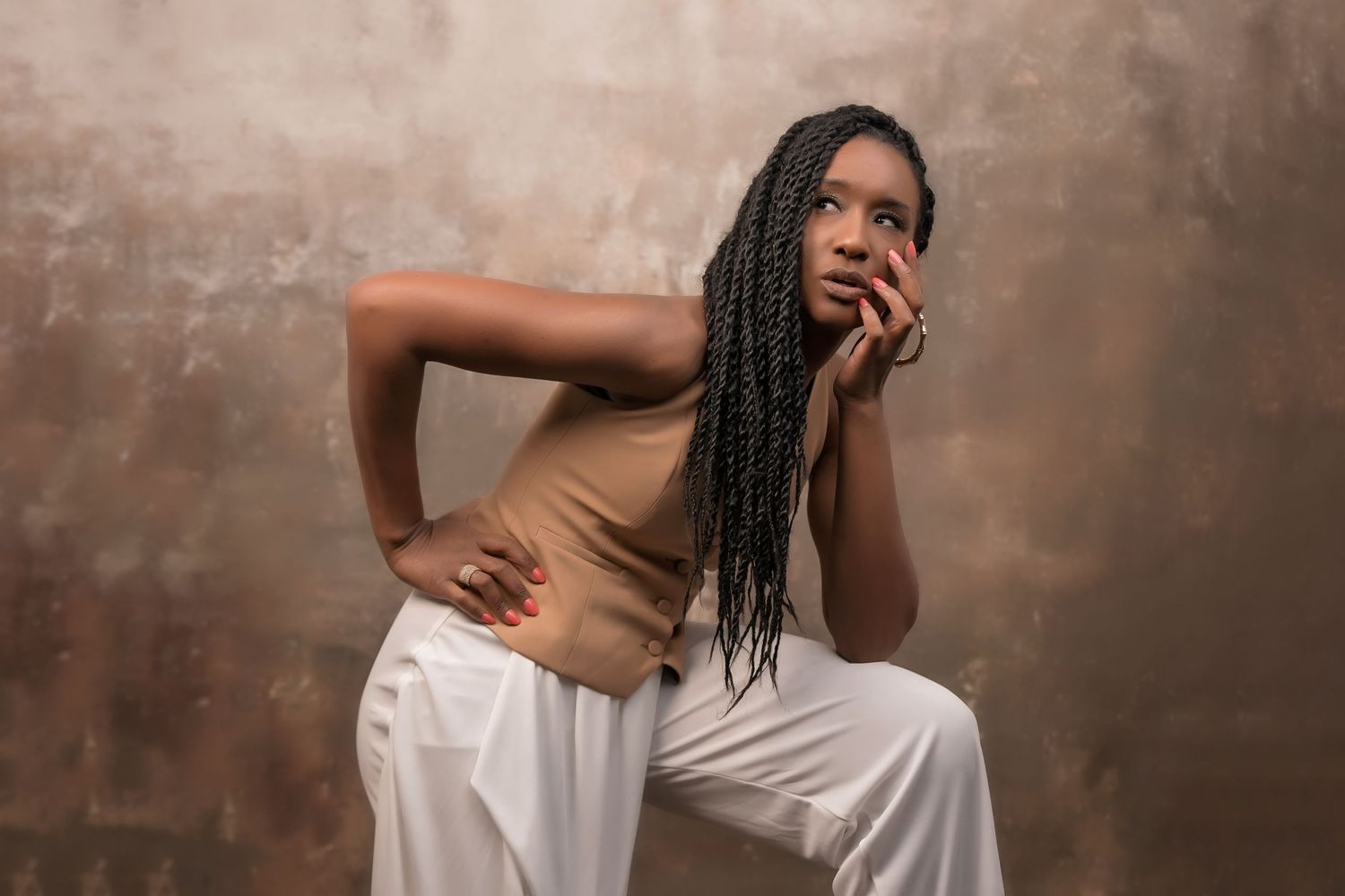 Studio portrait featuring woman in white and tan outfit posed against mottled brown backdrop
