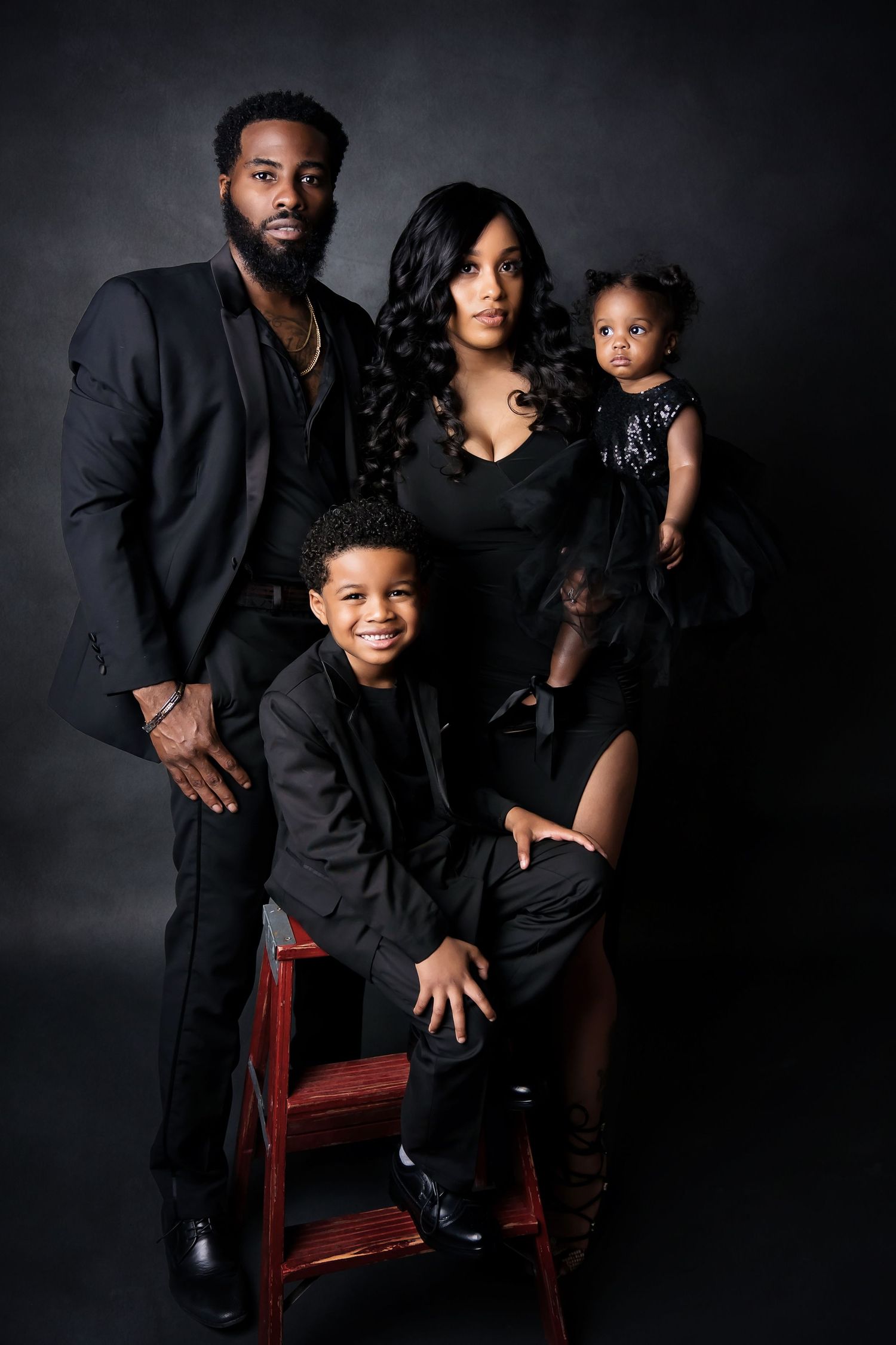Family of three posing together in coordinated outfits against a dark studio backdrop