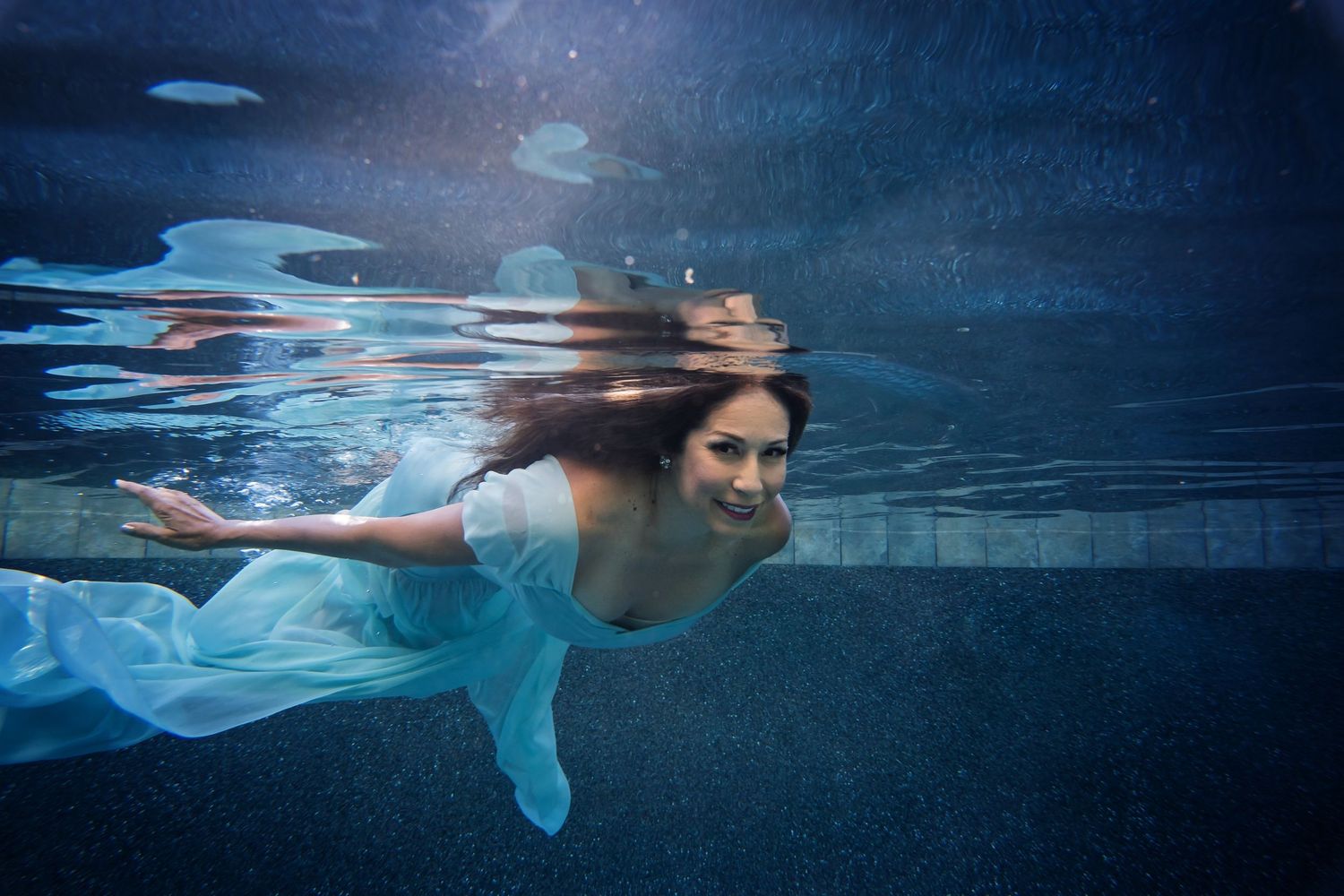 Artistic underwater portrait with elegant dress flowing through deep blue water