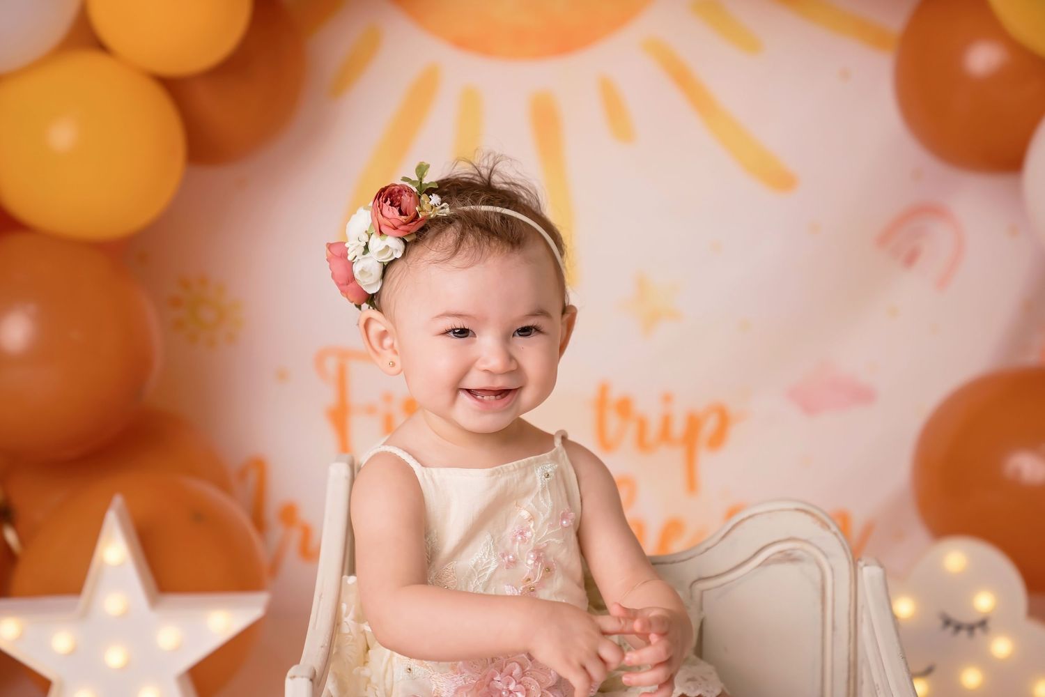 Warm-toned photoshoot setup with orange balloon arch and sun illustration backdrop.