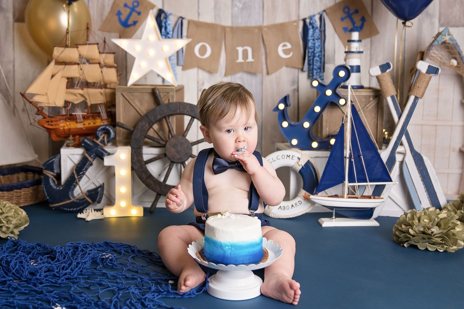 Cake smash photo session with nautical decorations featuring navy blue and gold party elements in san diego cake smash photography studio