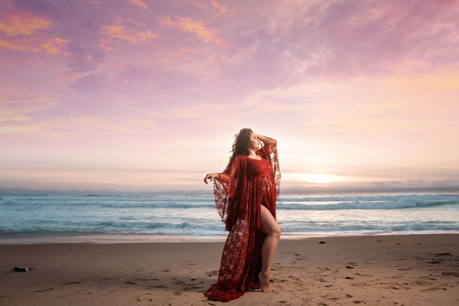 Romantic beach maternity photography with flowing red dress against vibrant sunset sky. San Diego Maternity Photographer