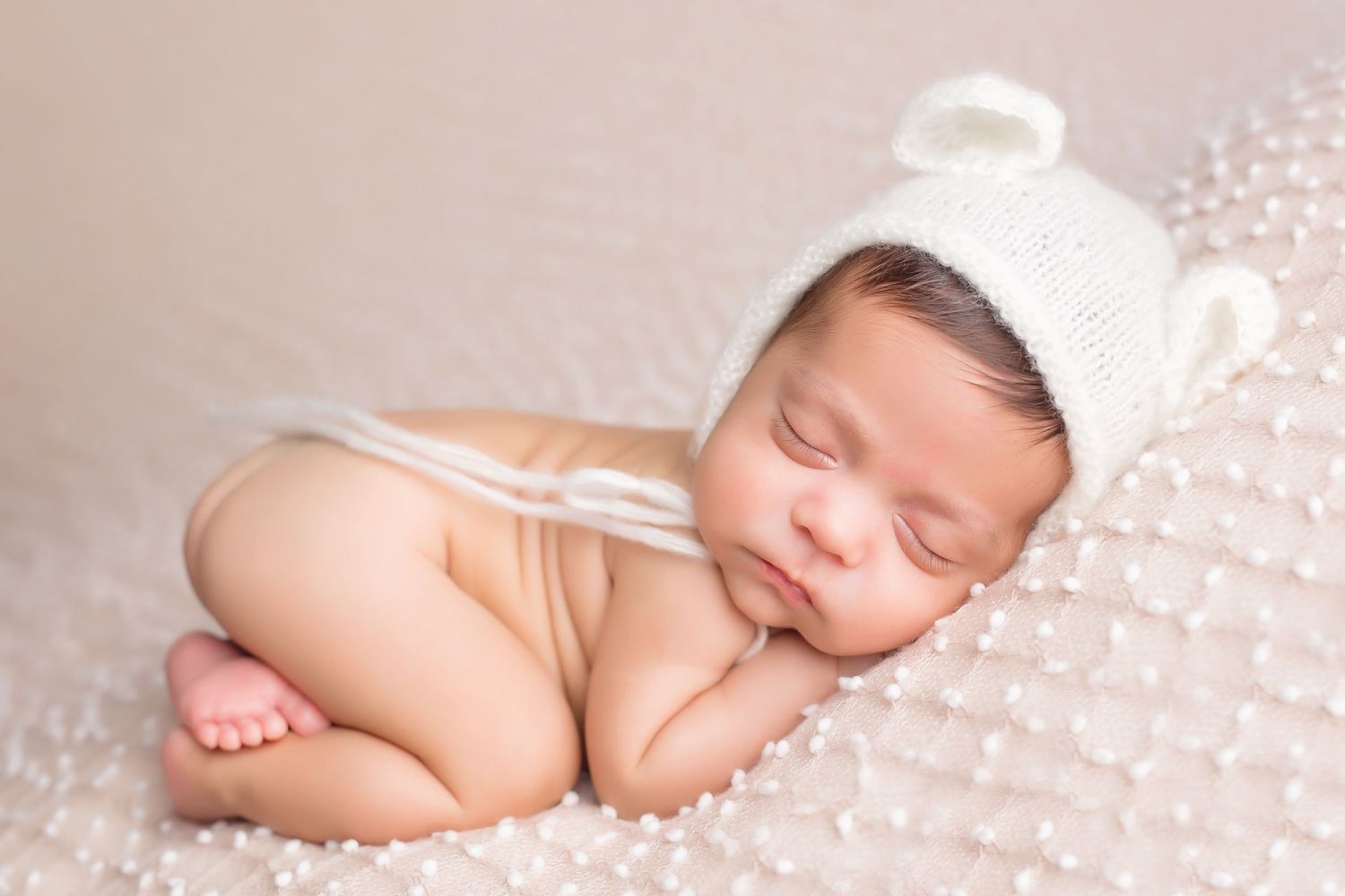 Peaceful newborn sleeping on textured white blanket during professional photo session. San Diego Newborn Photographer