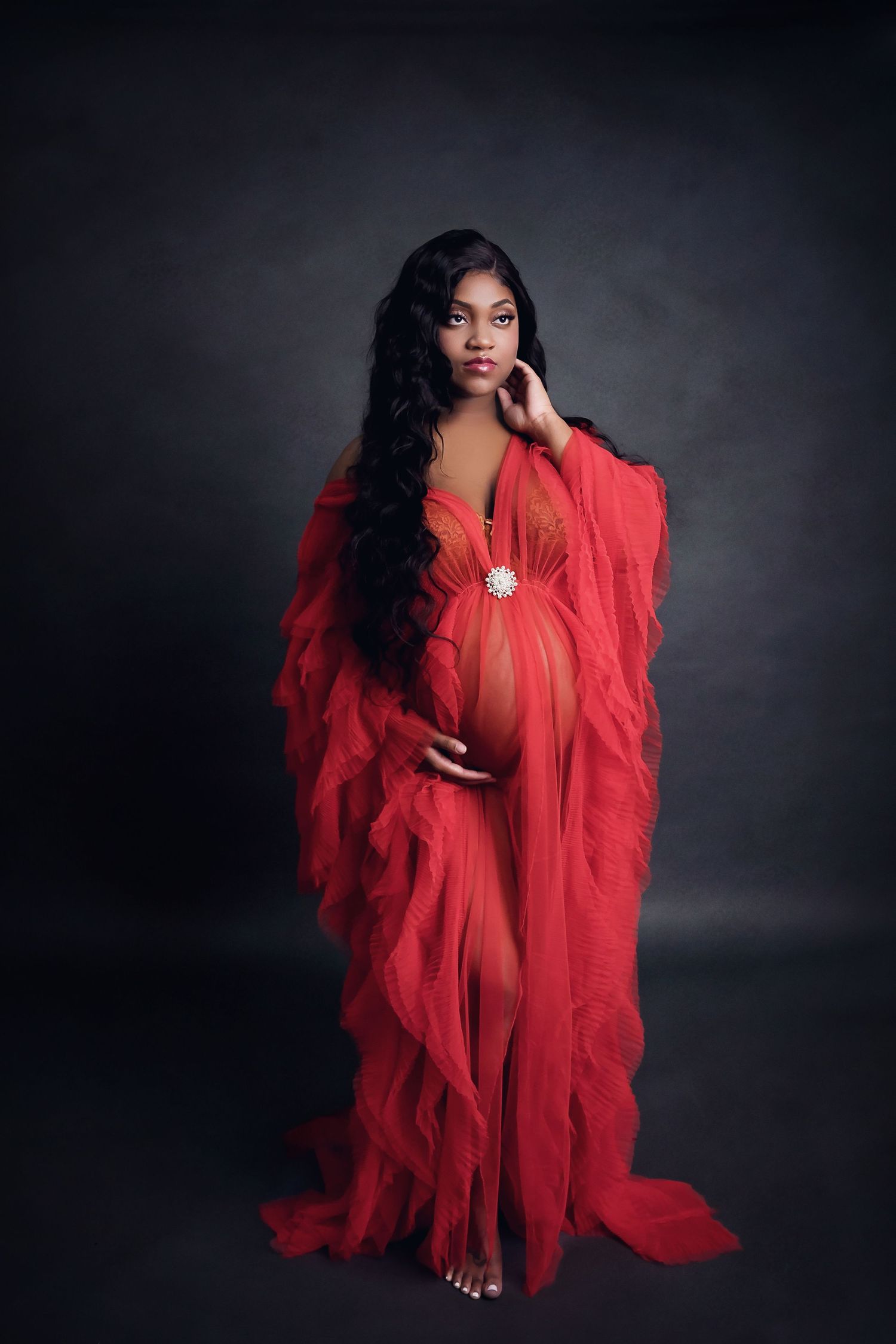 Ethereal maternity portrait in flowing red sheer gown against dark background.