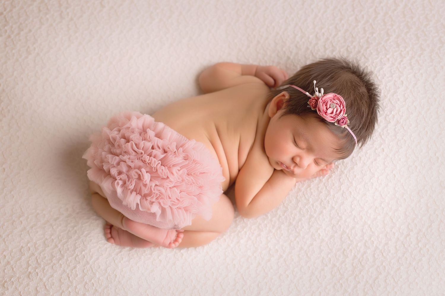 Newborn baby in pink tutu sleeping on white backdrop in artistic pose. San Diego Newborn Photographer