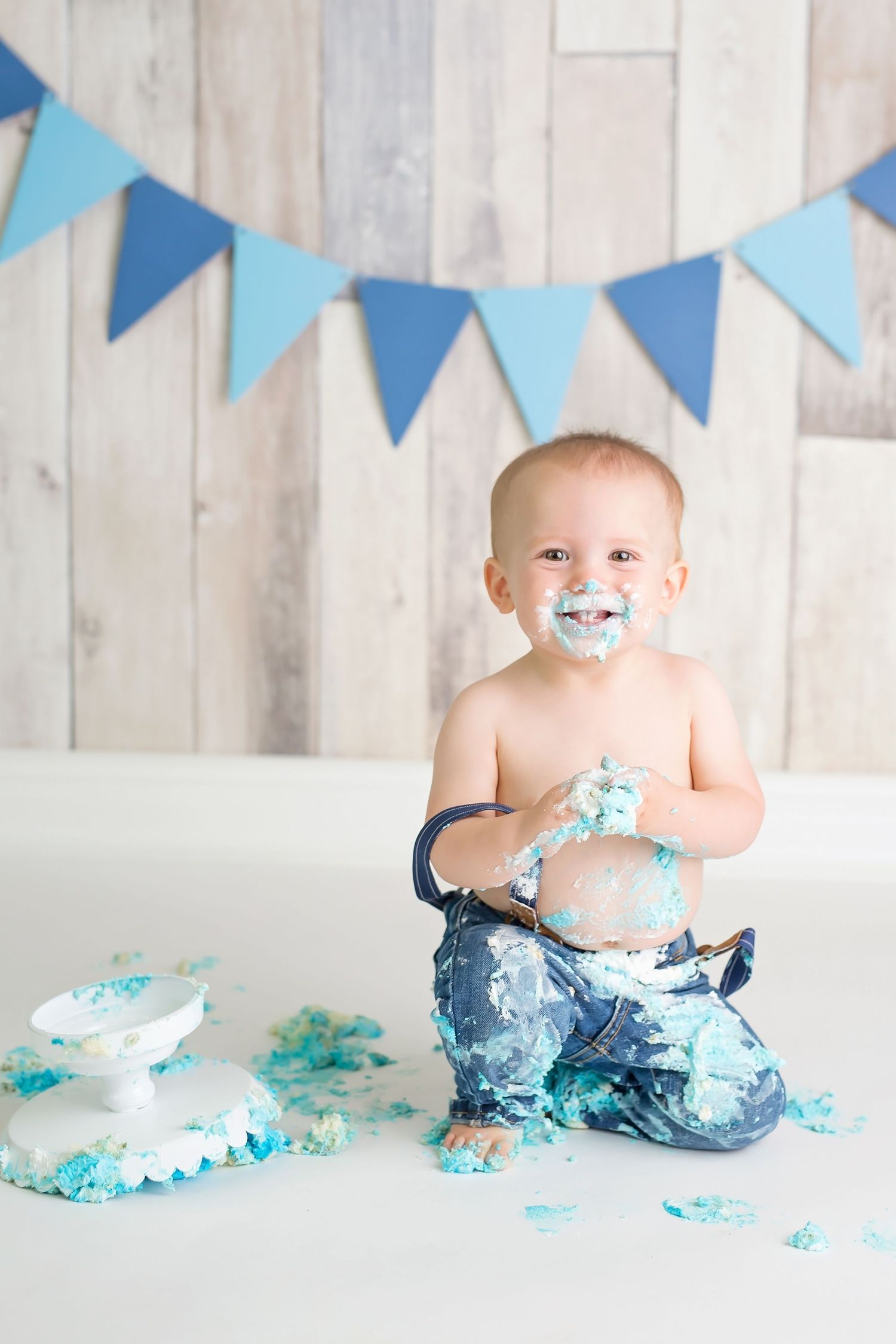 Blue cake smash photo session with bunting flags and turquoise frosting on white wooden backdrop. San Diego cake smash photographer