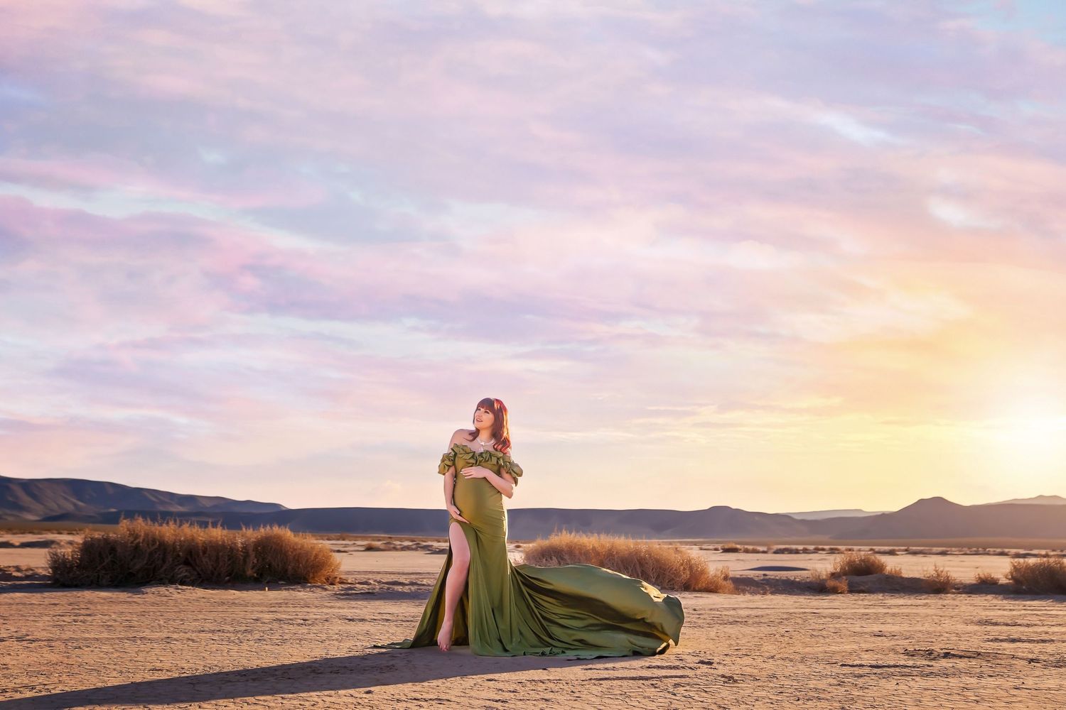 Flowing green dress creates dramatic maternity silhouette against desert sunset landscape. San Diego Maternity Photographer