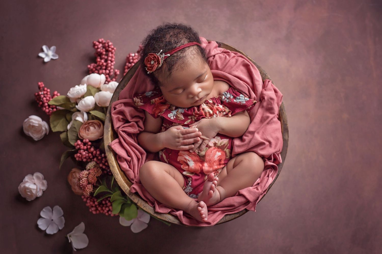 Newborn sleeping in round basket surrounded by pink fabric and white floral decorations. San Diego Newborn Photographer