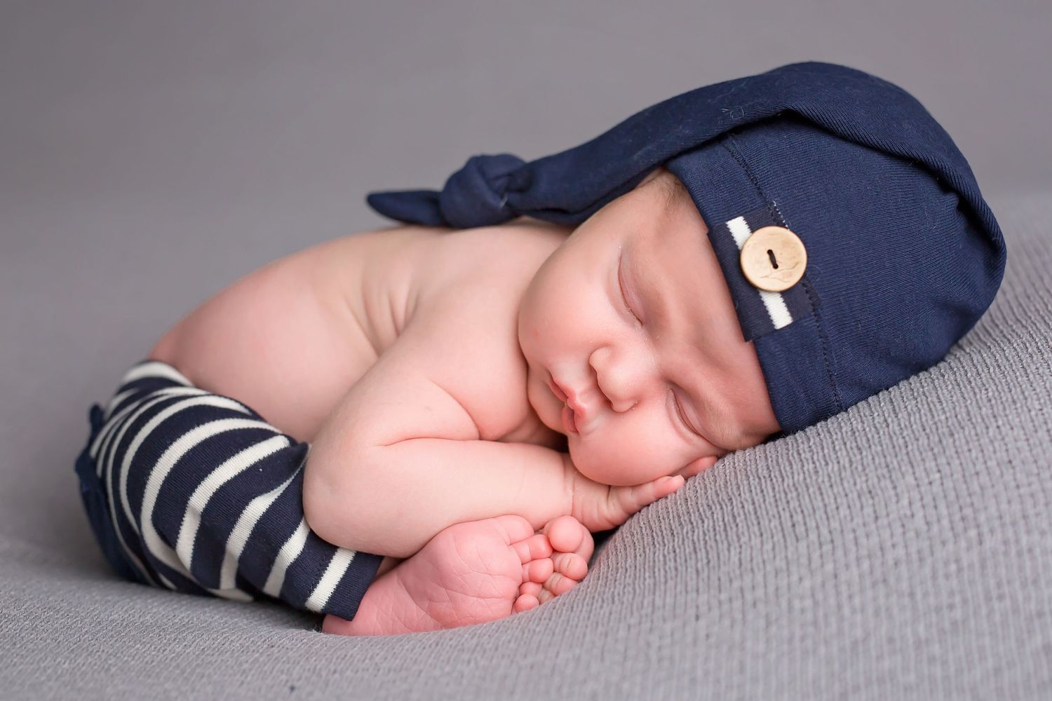 Sleeping newborn wearing navy blue hat and striped outfit rests on grey blanket in professional portrait series. San Diego Newborn Photograp