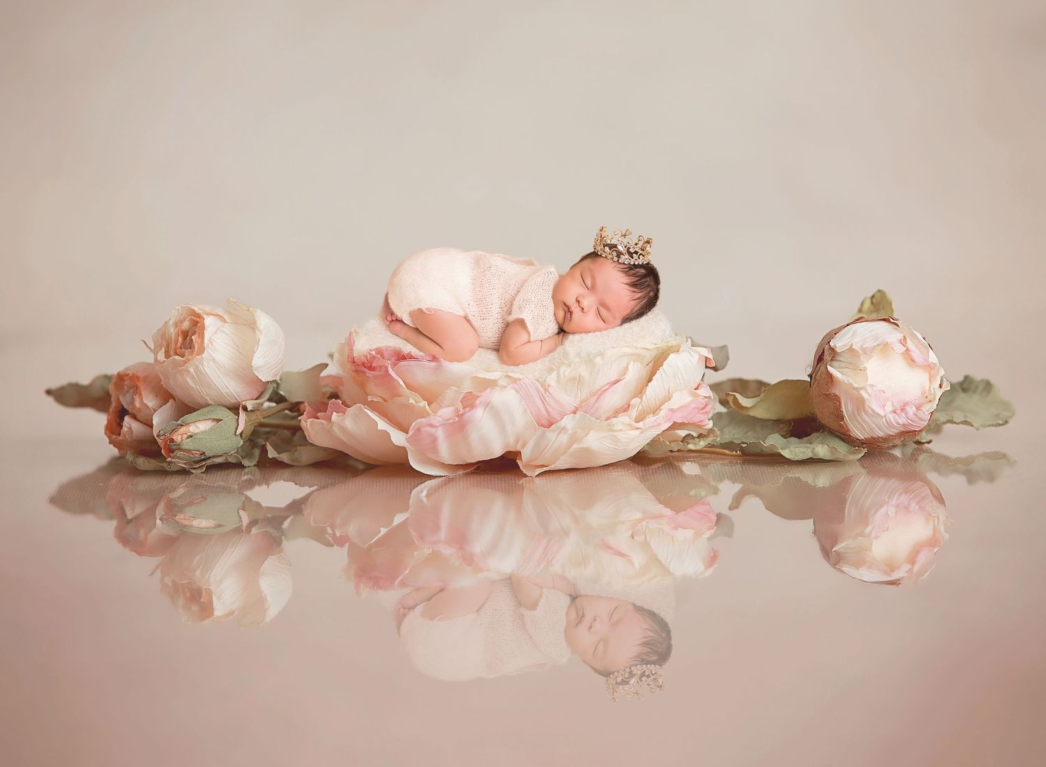 San Diego newborn photographNewborn baby sleeping peacefully in pink floral setup with roses creating dreamy reflection on mirrored surface.