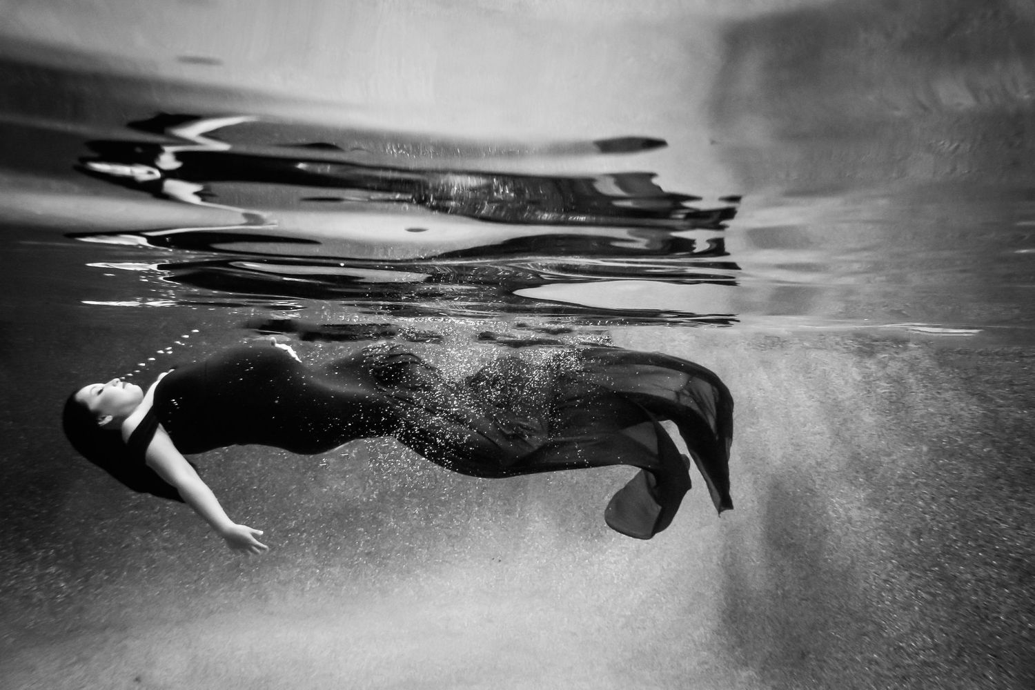 Monochrome underwater portrait showing silhouetted figures and rippling water texture