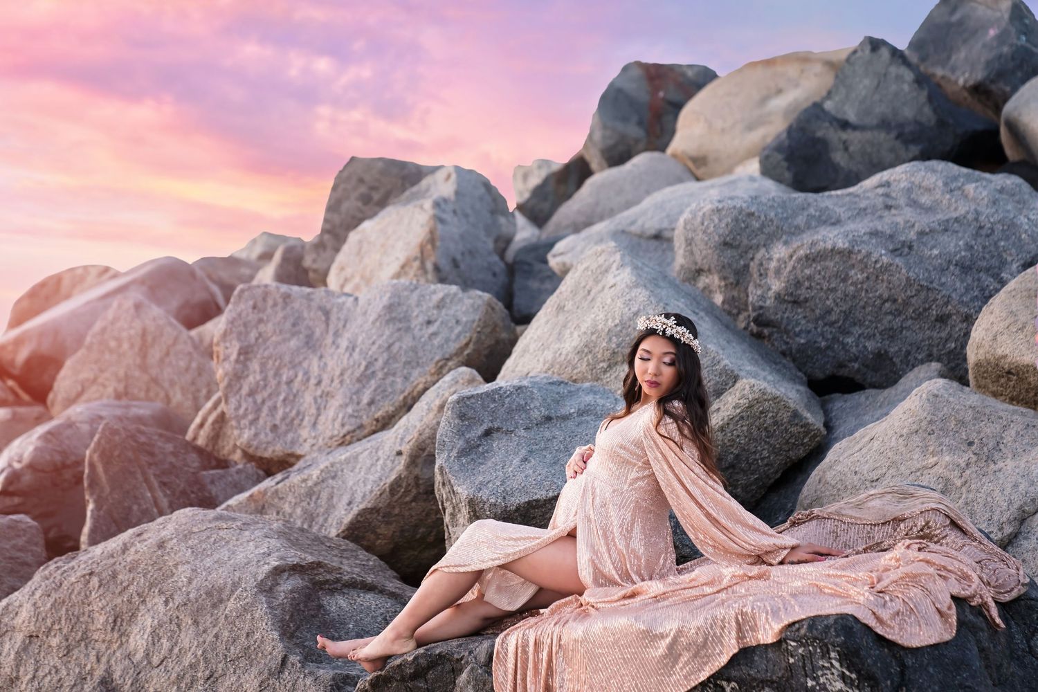 A pink flowing gown drapes over coastal rocks during a dreamy sunset photoshoot. San Diego Maternity Photographer