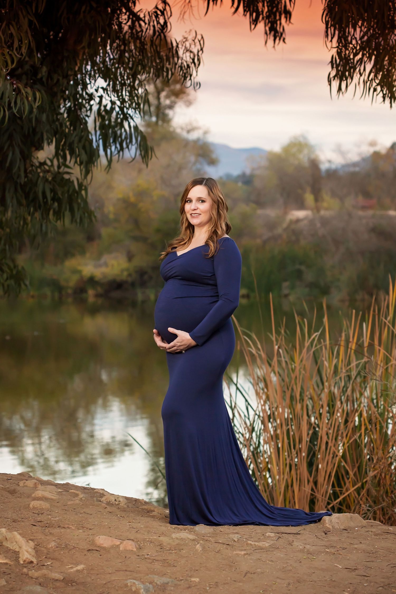 Maternity session by a lake with navy blue dress and natural reed backdrop. San Diego Maternity Photographer