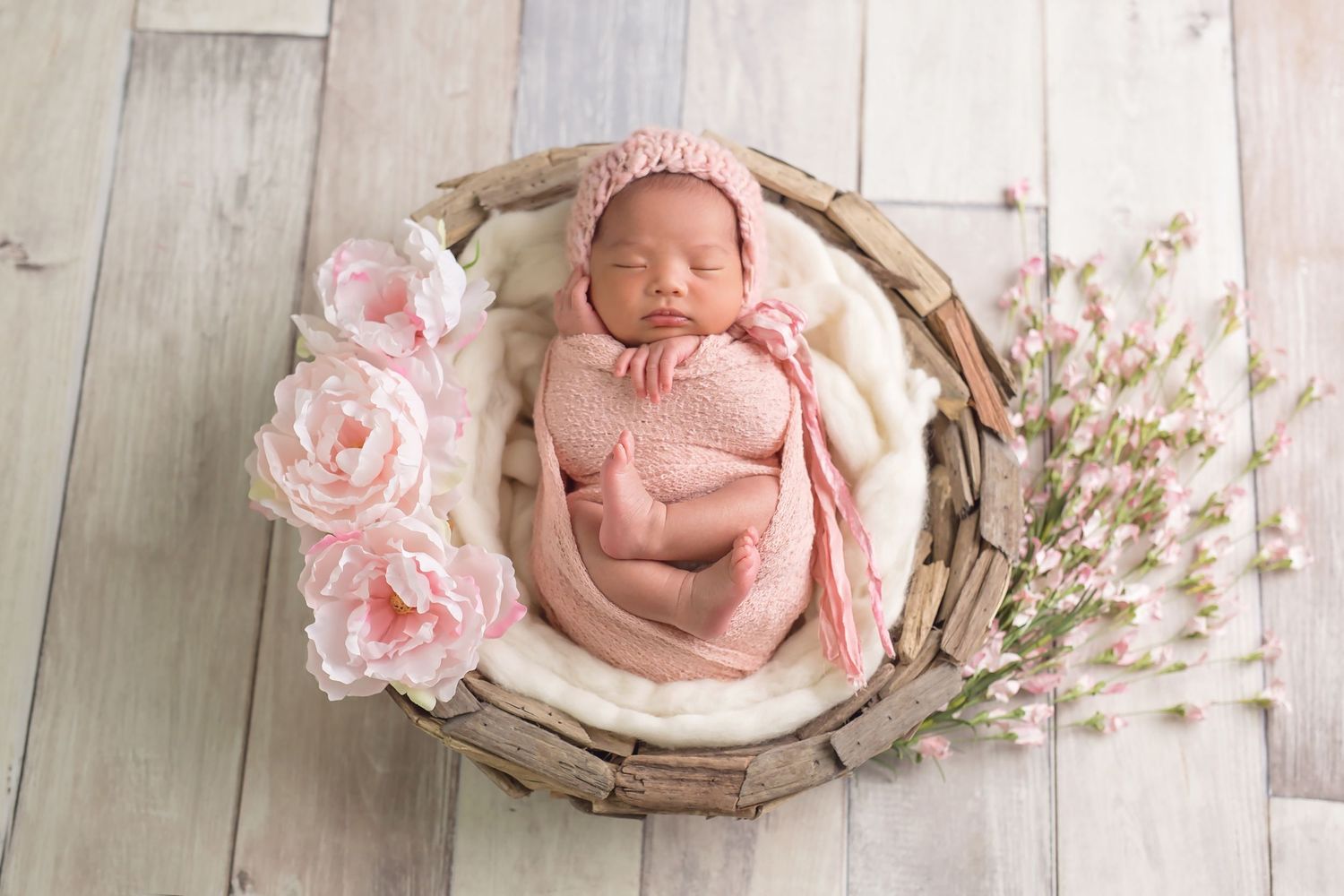 Sleeping newborn wrapped in pink blanket with delicate floral decorations on wooden backdrop. San Diego Newborn Photographer