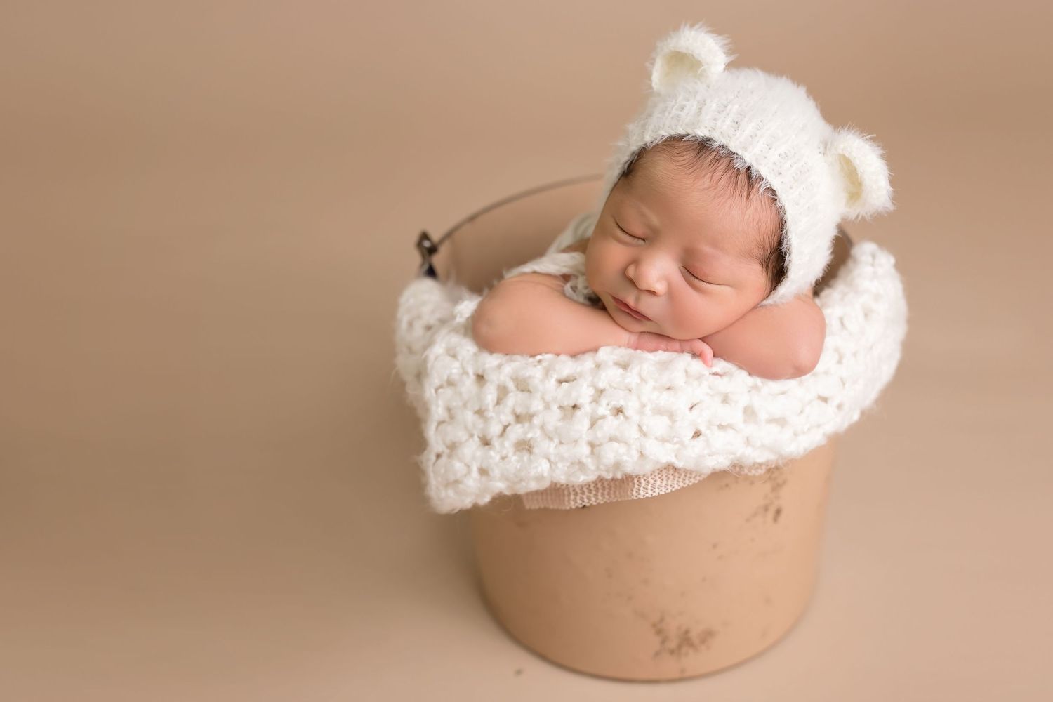 San Diego newborn photographer captures Baby sleeping in cream-colored bowl prop with white knit accessories.