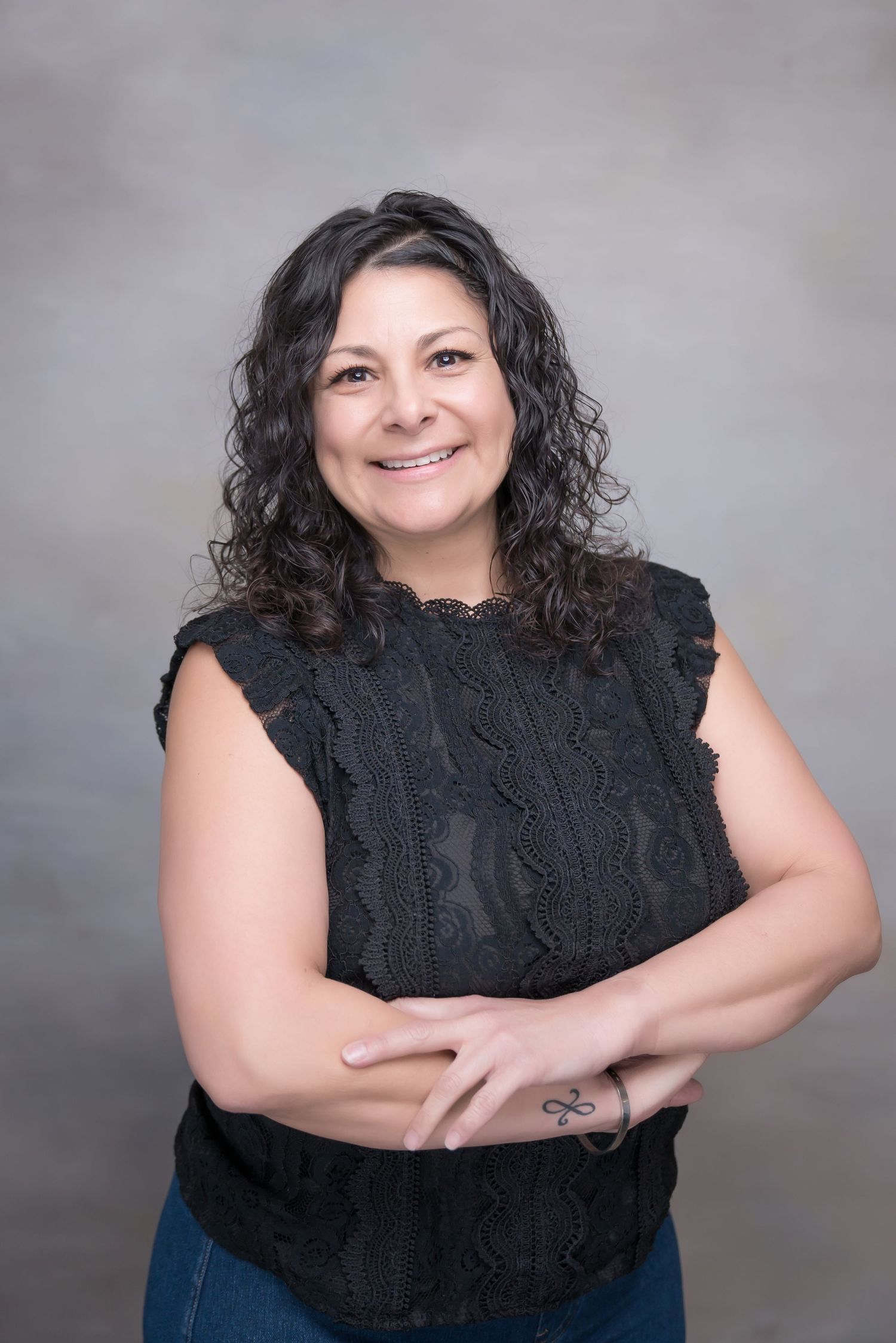 Studio headshot featuring woman with natural curls wearing black lace top against grey background