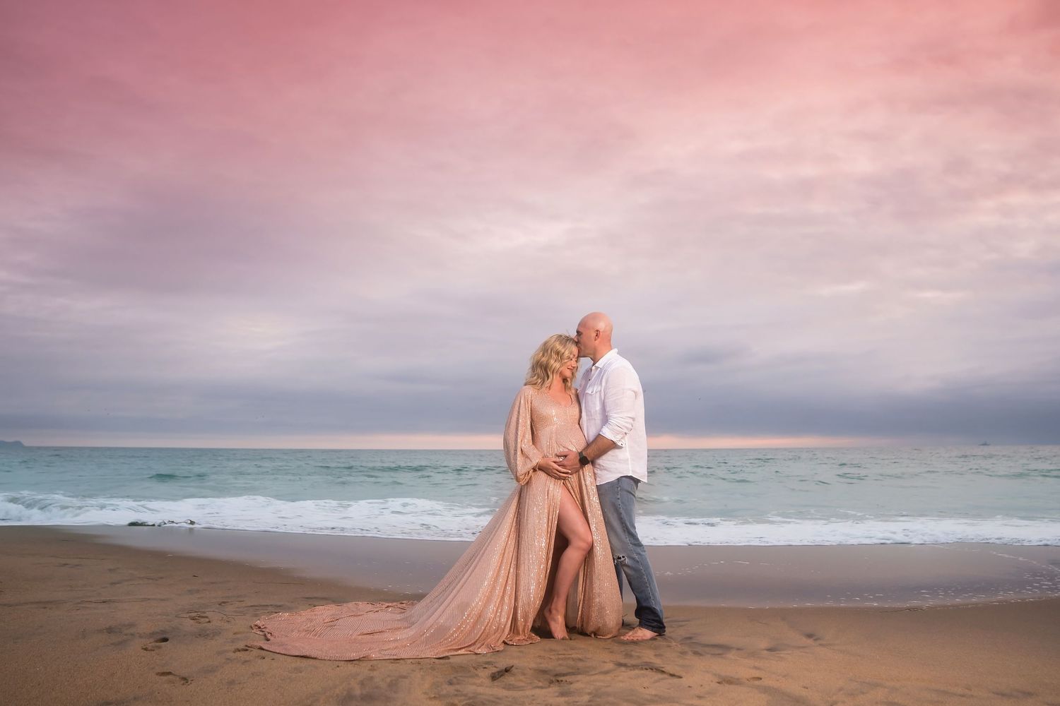 Romantic sunset beach maternity photoshoot with flowing dresses and rocky coastal backdrop. San Diego Maternity Photographer