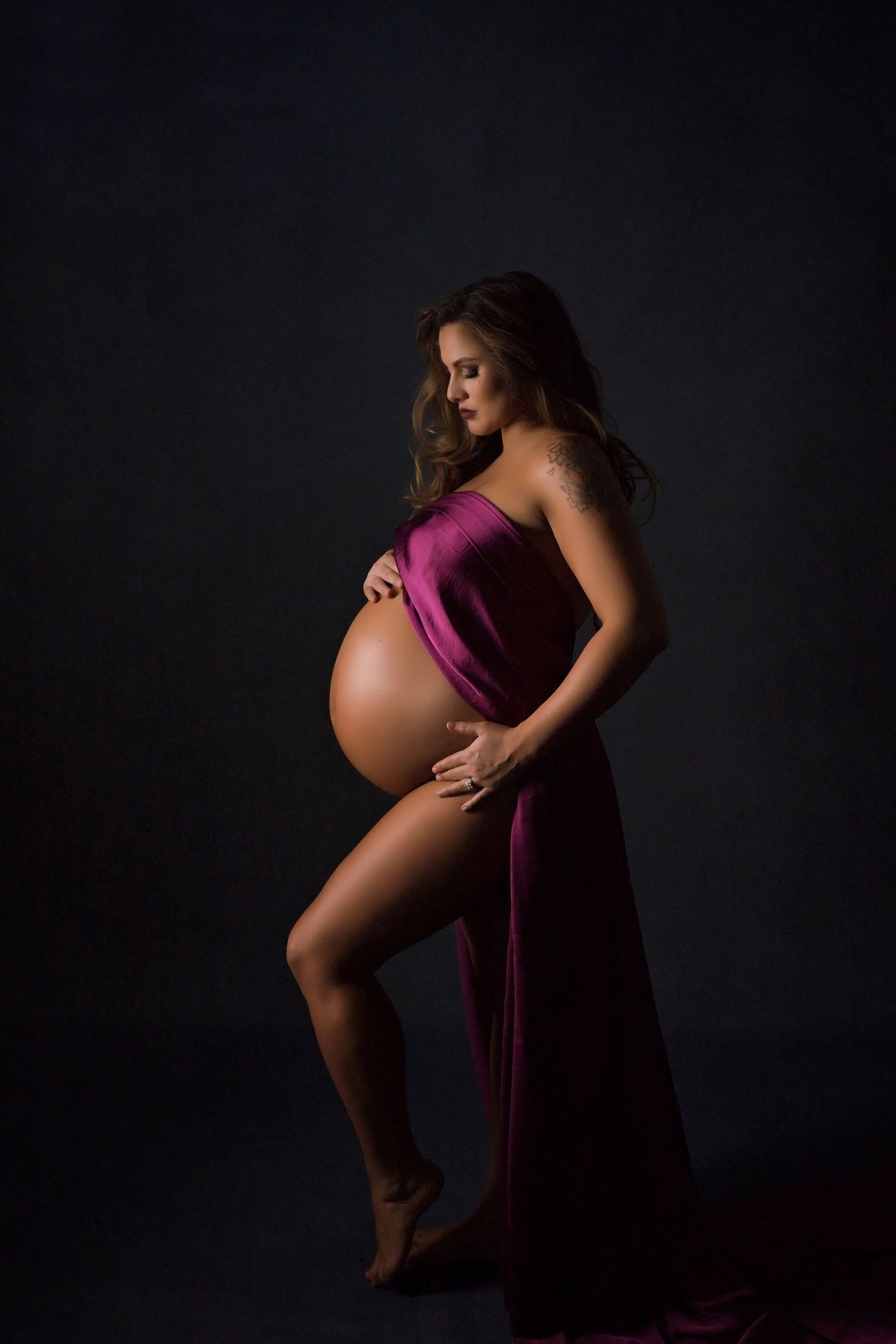 Moody maternity portrait with woman in deep purple flowing dress.