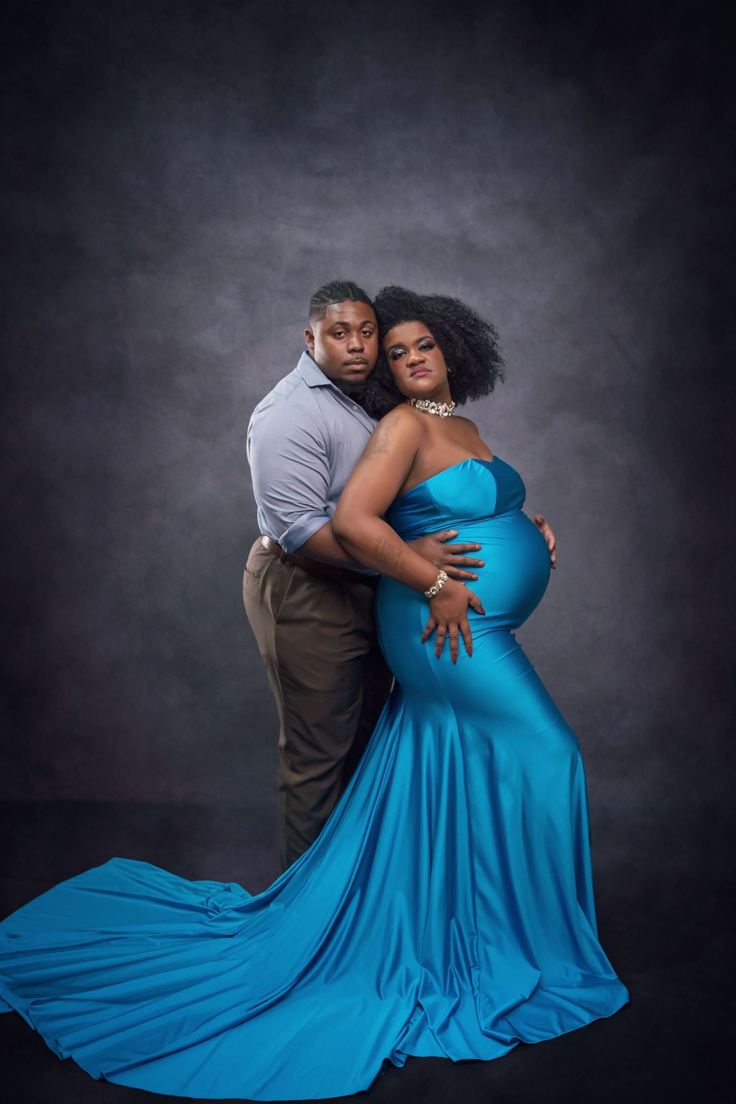 Couple’s maternity portrait with blue satin gown against dark backdrop