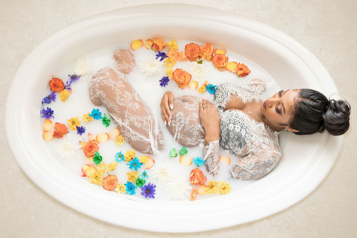 Milk bath maternity photo with colorful flowers and white lace dress.