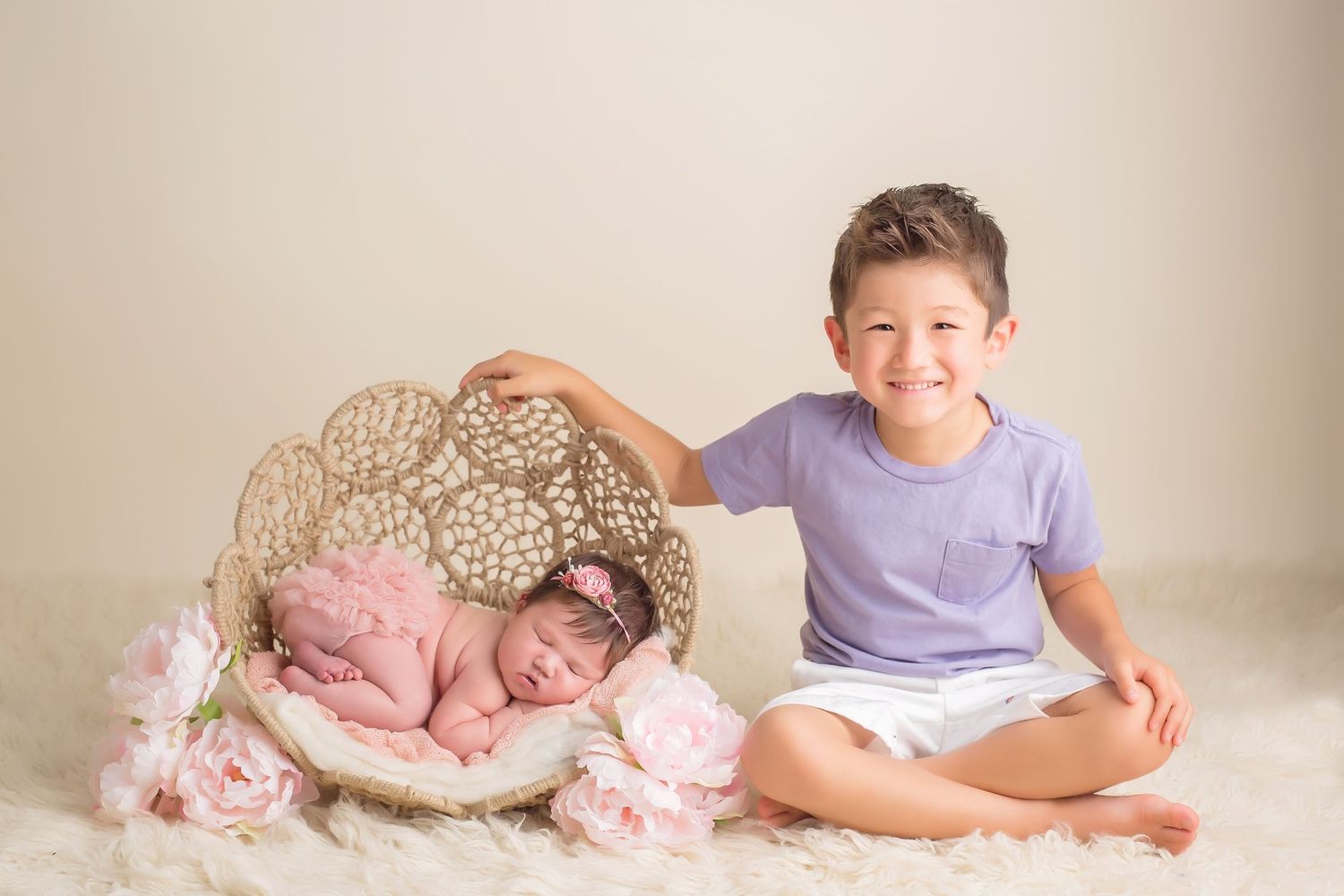 Siblings pose together during professional photo session against neutral background. San Diego Newborn Photographer