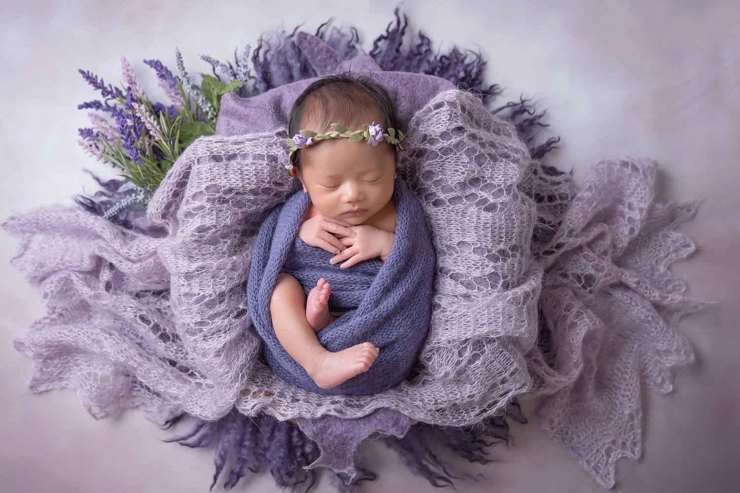 Baby wrapped in purple textured fabric with lace accents in studio setting. San Diego Newborn Photographer