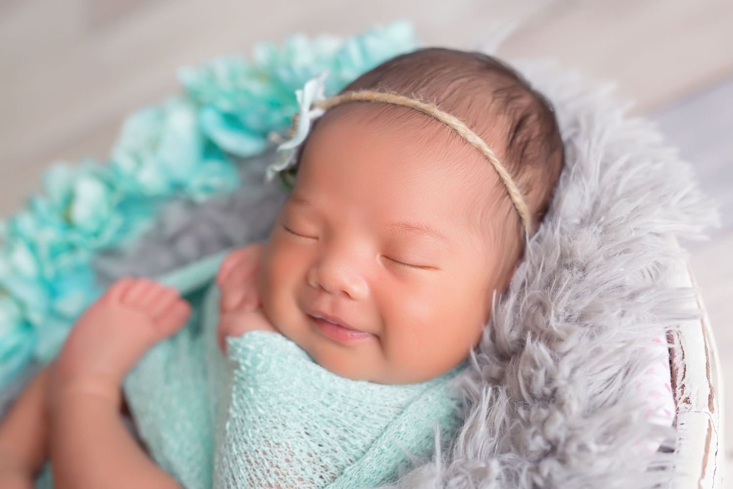 Sleeping baby in mint green wrap posed with gray fur during professional newborn photography. San Diego Newborn Photographer