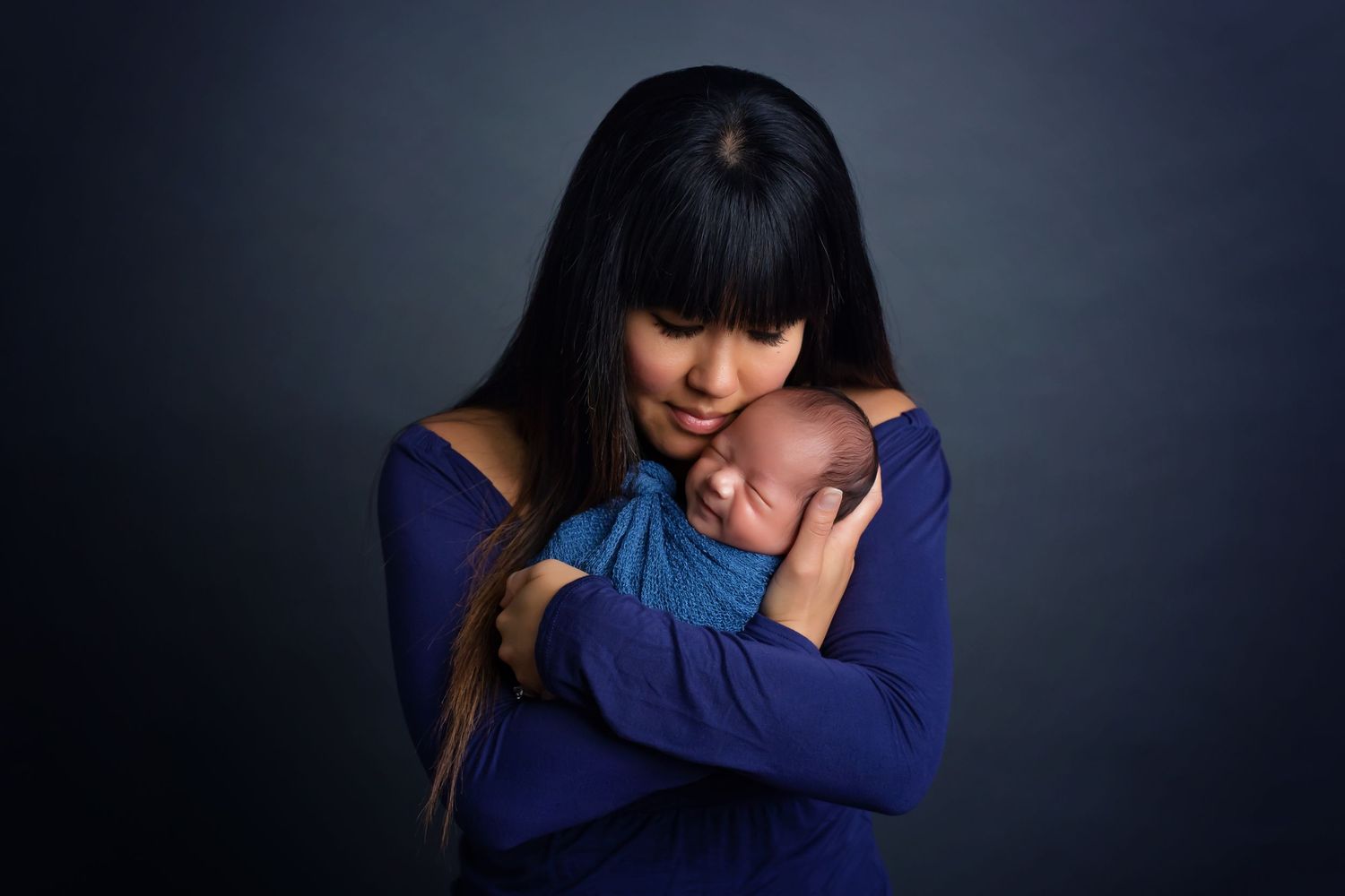San Diego newborn photographer captures Artistic portrait of mother with smiling newborn in coordinating blue outfits
