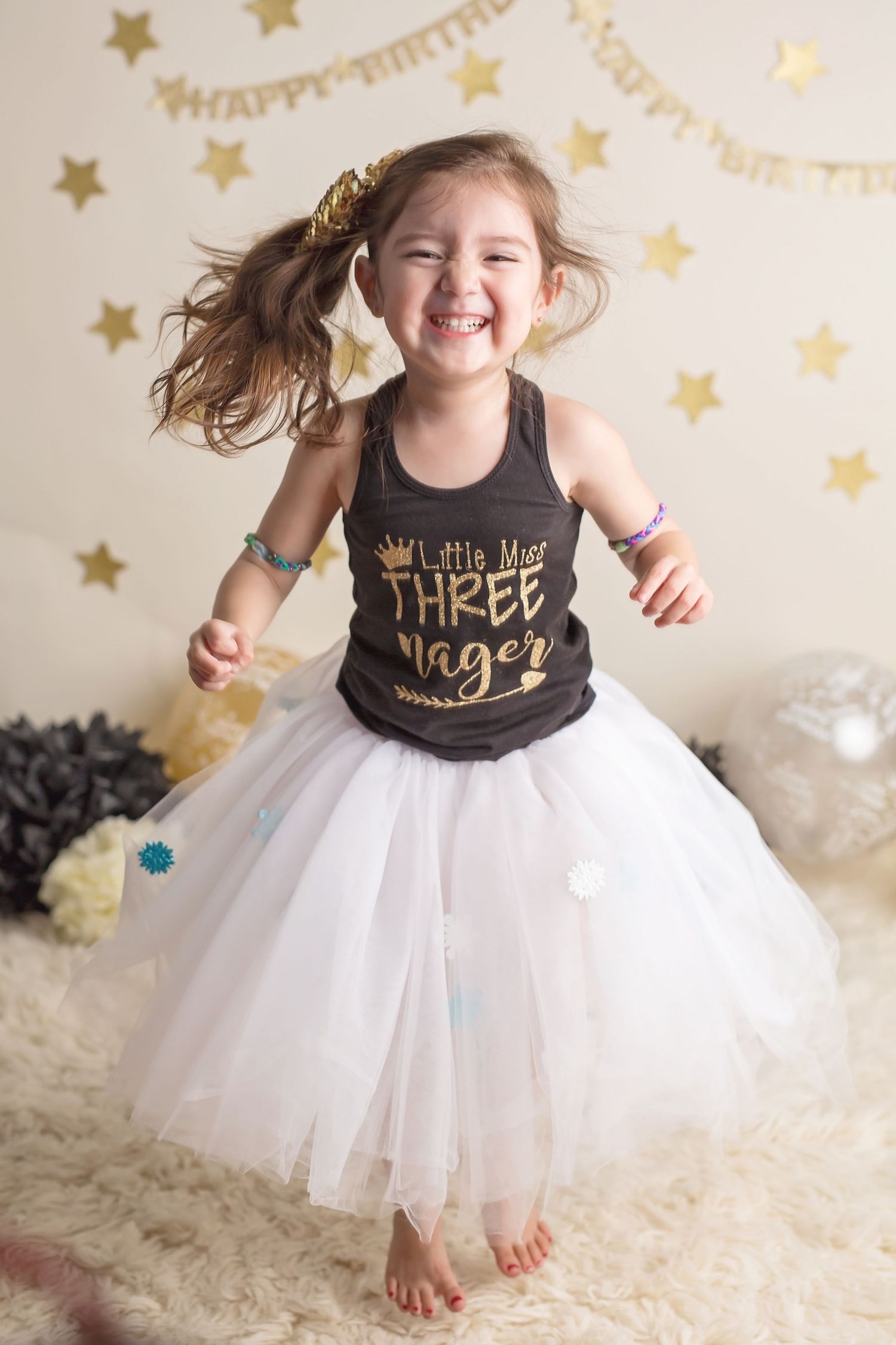 Child twirling in white tulle skirt against gold star backdrop for celebration photos.