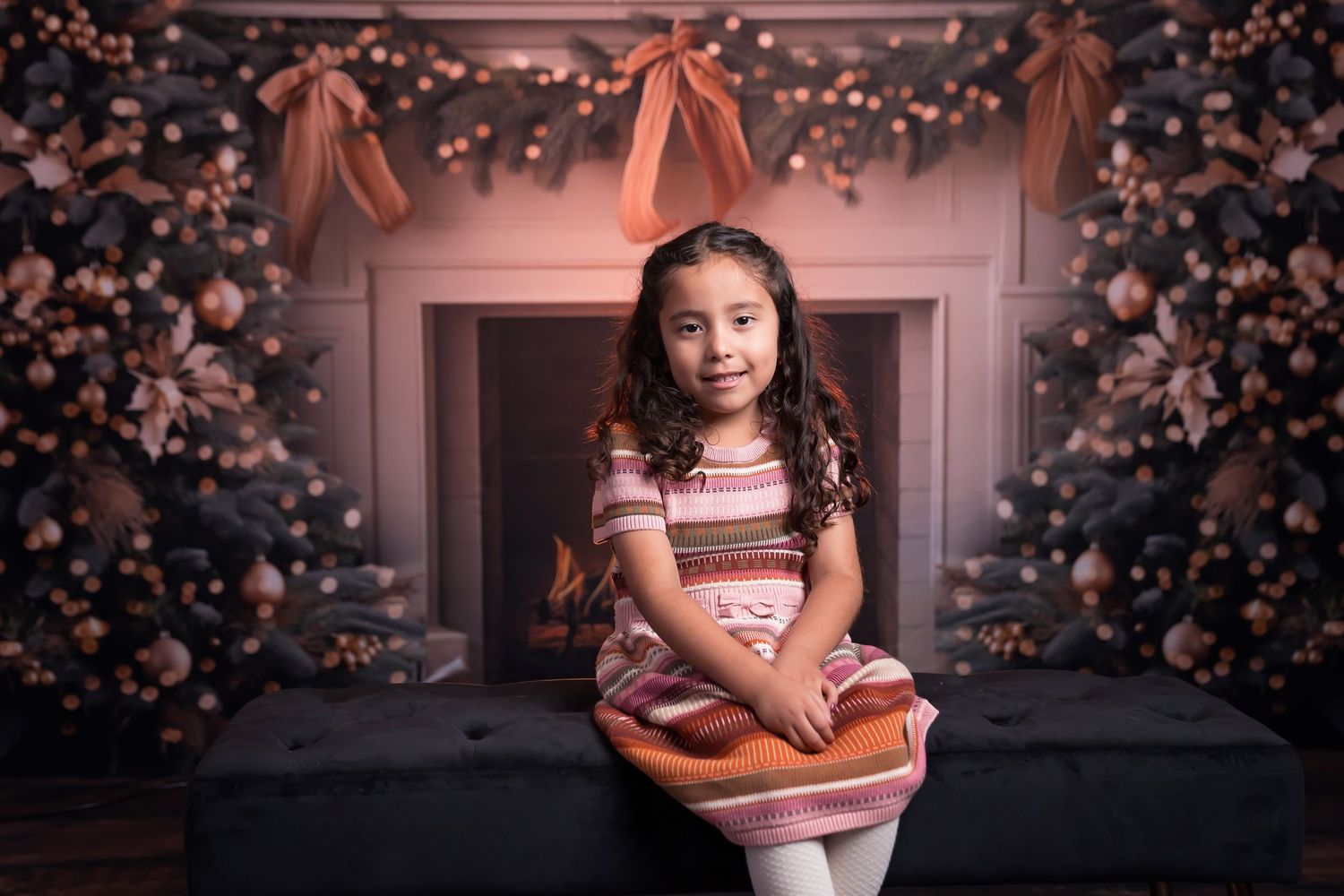 San Diego Mini holiday session. Young child in striped dress poses in front of decorated holiday fireplace with bokeh lights.