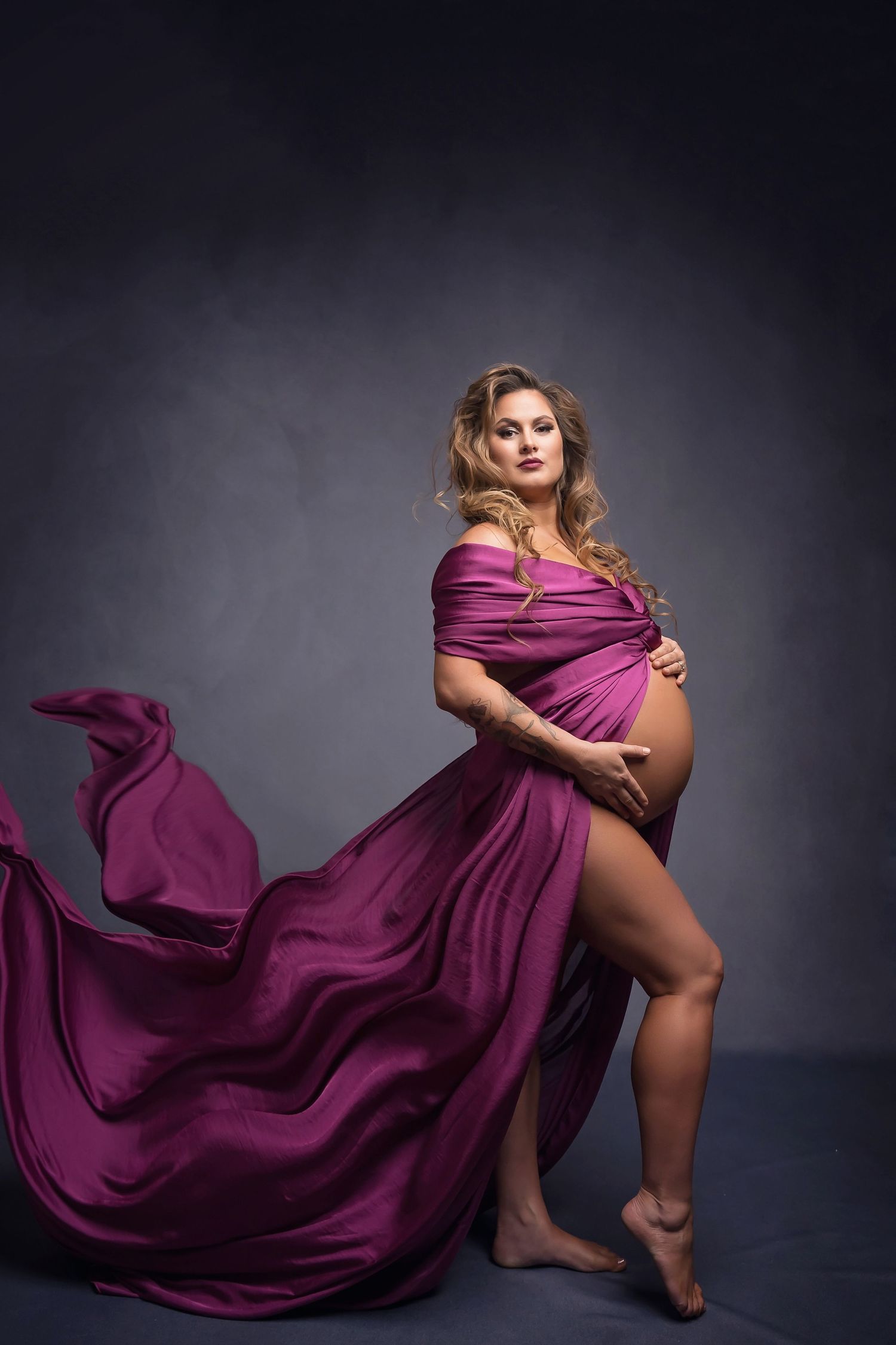 Dramatic maternity photo with flowing magenta dress against dark background.