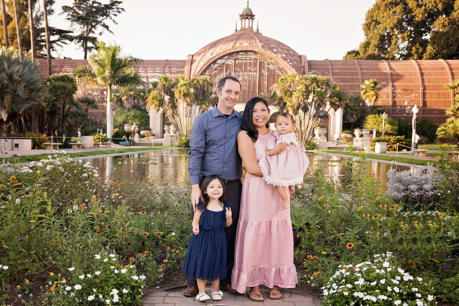 Family posing outdoors in front of an ornate botanical garden building with reflecting pool and flowers