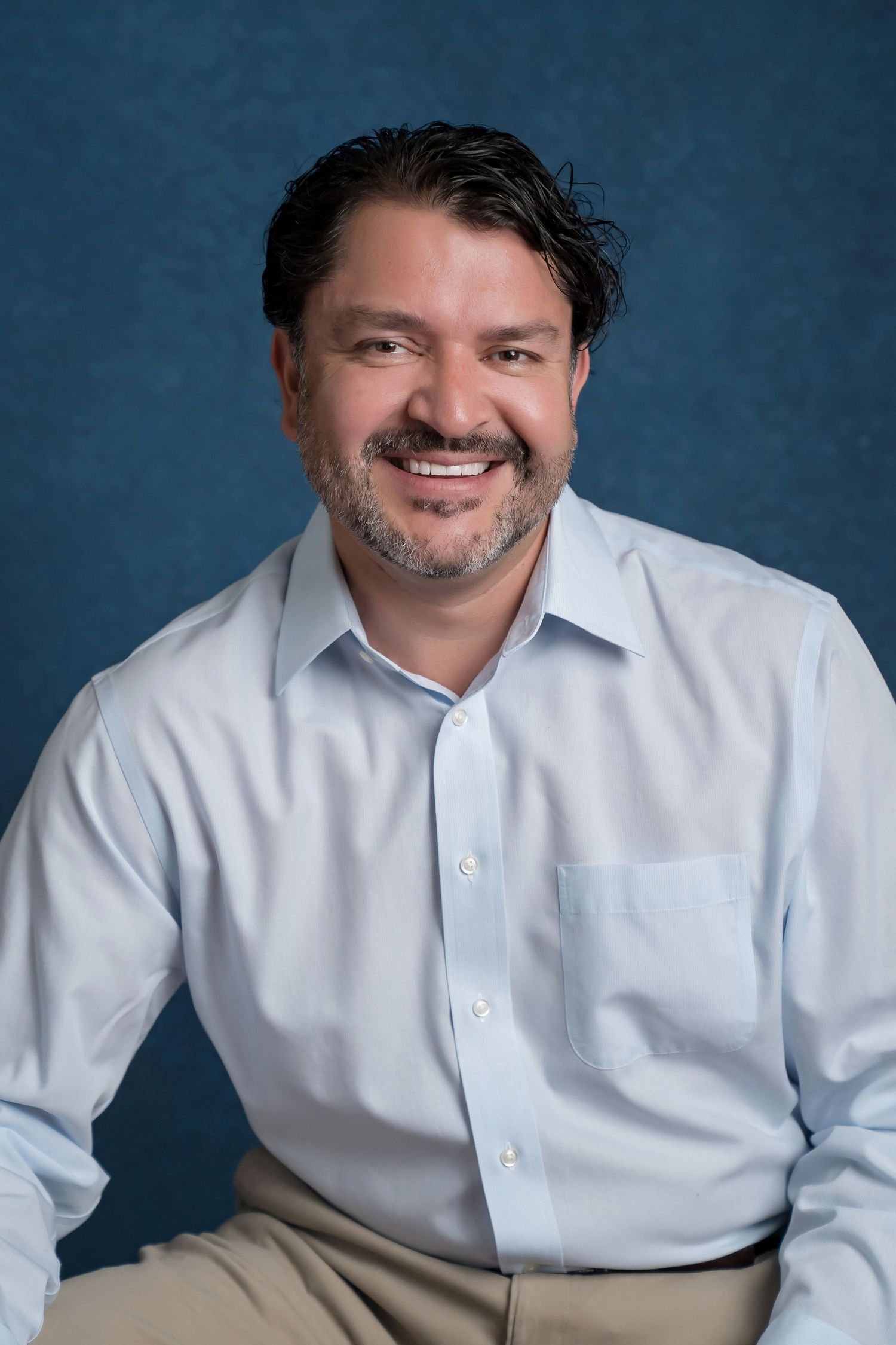 Corporate headshot of man in white button-down shirt against soft blue backdrop
