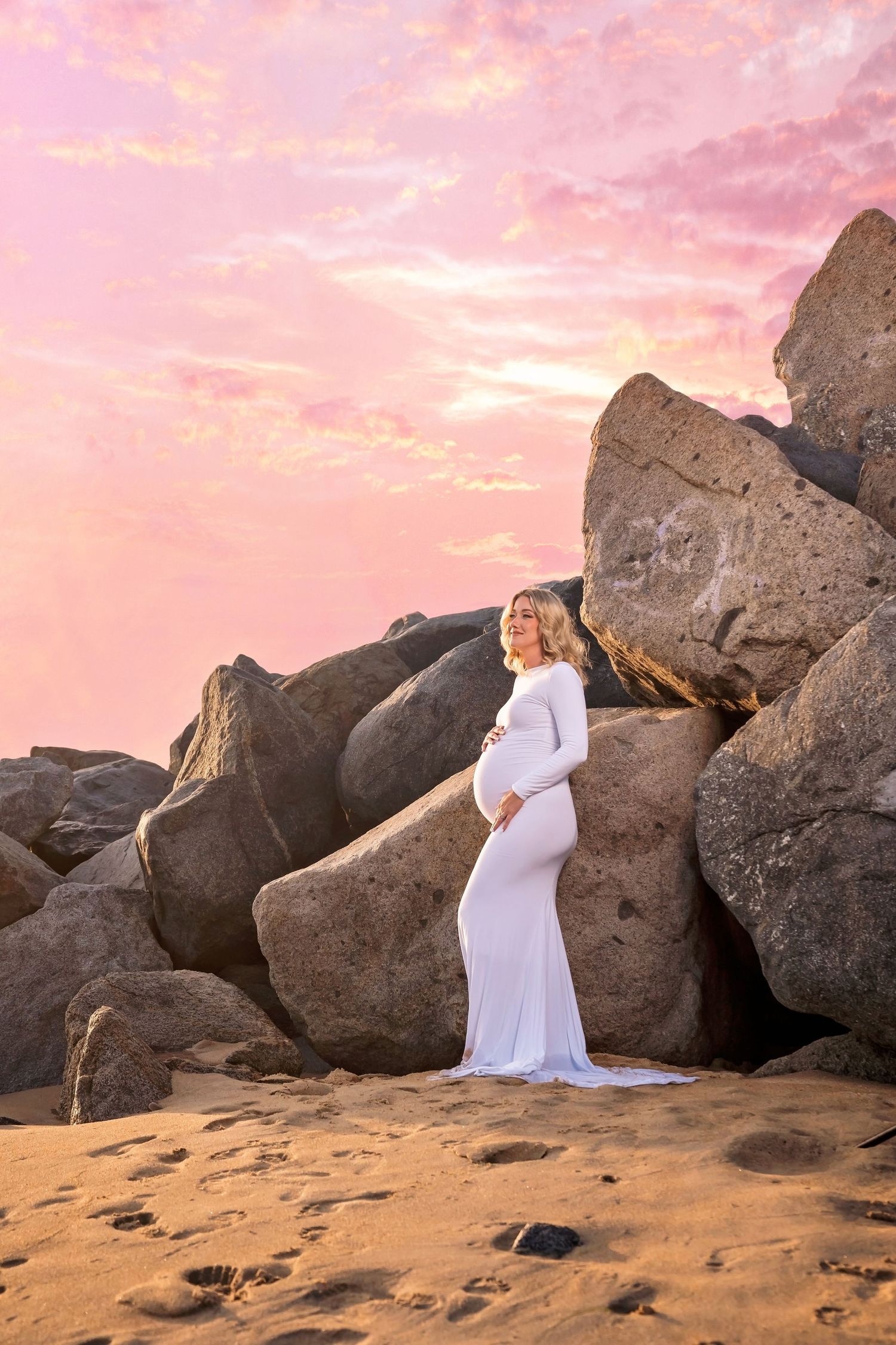 Maternity photos against large coastal rocks during pink sunset. San Diego Maternity Photographer