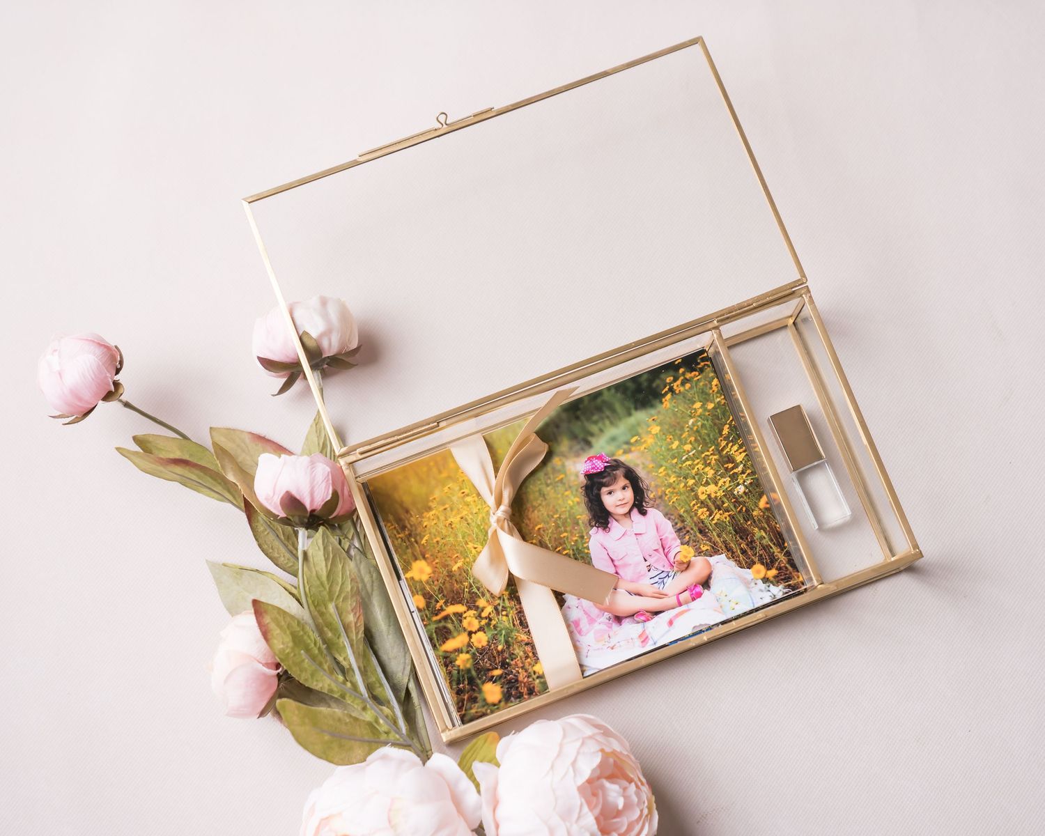 Glass photo box with floral photo display and delicate pink peonies arranged beside it.