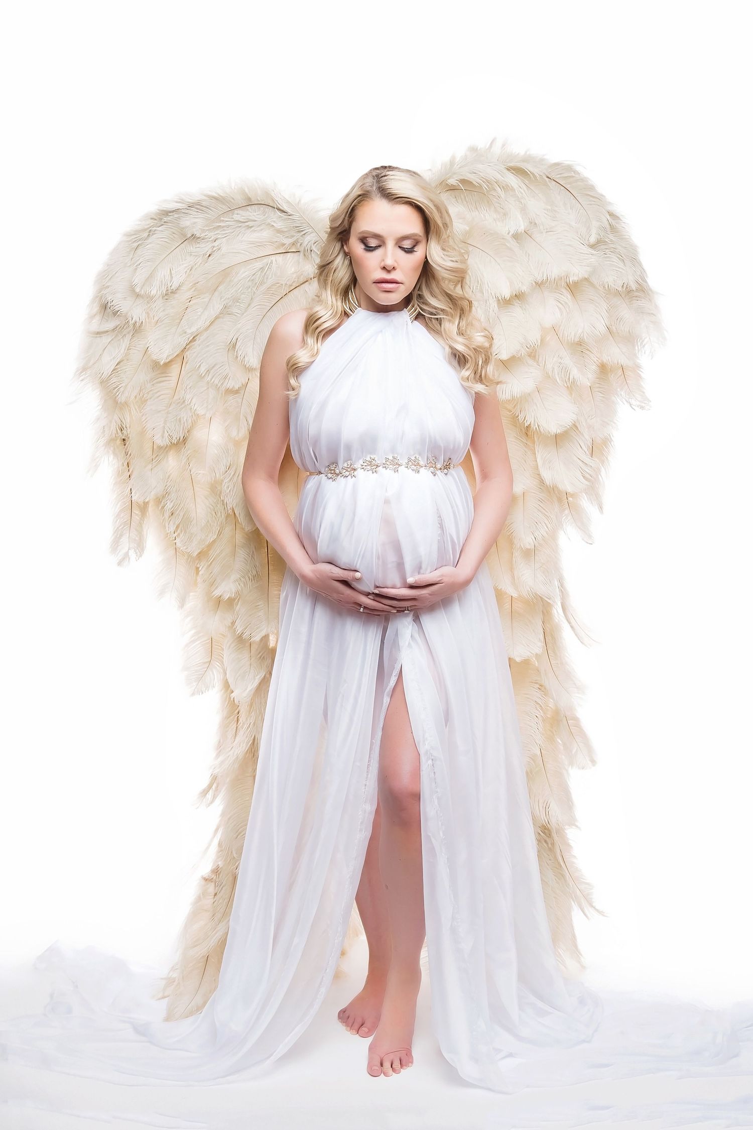 Angelic maternity portrait with large feather wings and soft white drapery