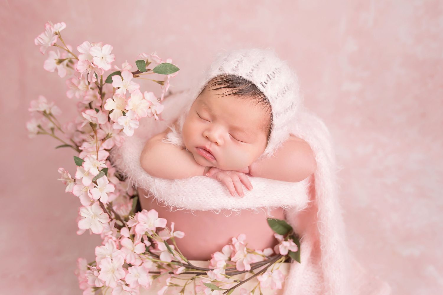 San Diego newborn photographer captures Peaceful newborn portrait with delicate pink cherry blossoms against soft pink background.