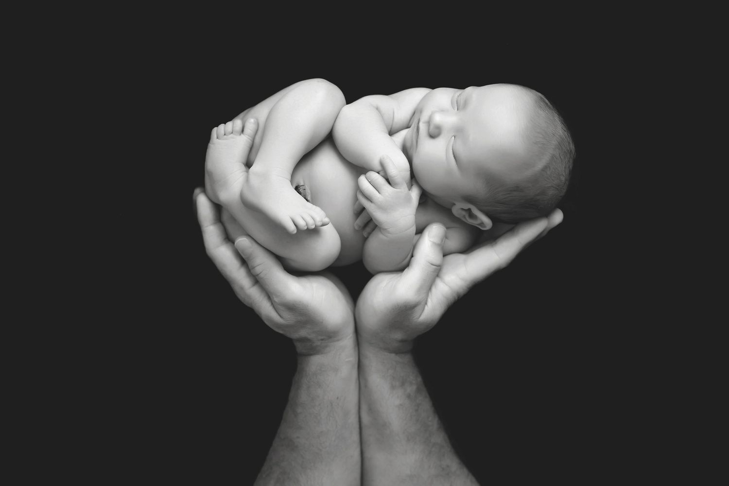 Dramatic black and white portrait of hands holding sleeping newborn. San Diego Newborn Photographer