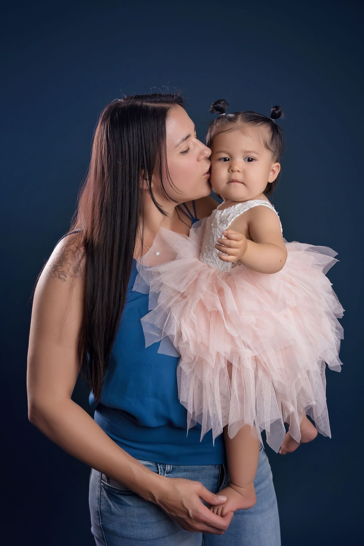 Sweet family moment against a dark blue studio backdrop with pink tulle dress details