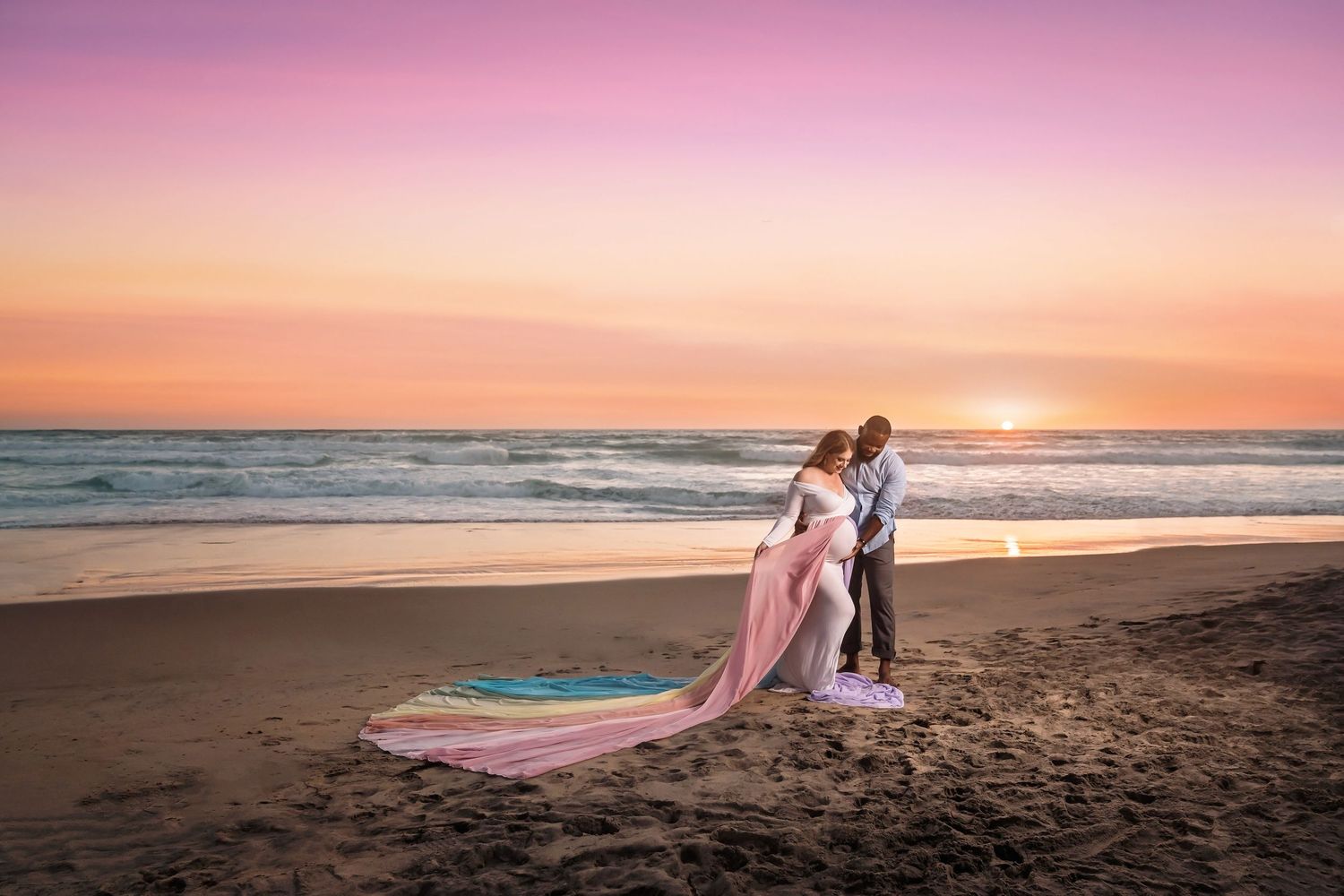 Rainbow baby maternity Beach session with flowing fabrics against pink and orange sunset sky. San Diego Maternity Photographer