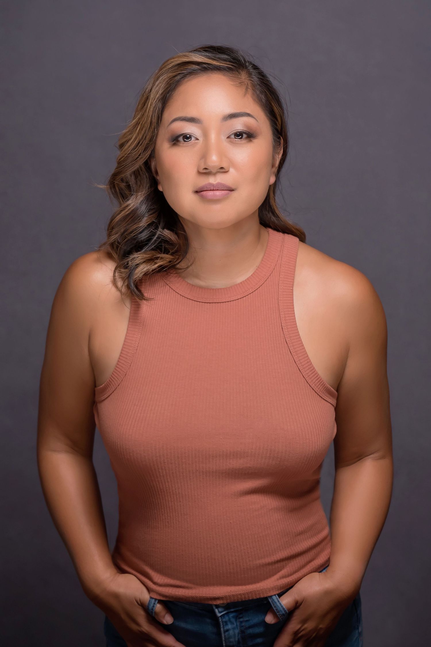 Studio portrait of woman in coral tank top posed casually against dark background