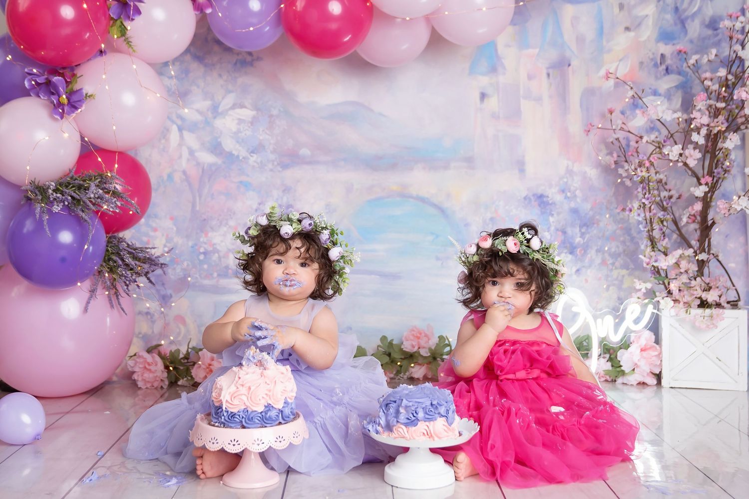 colorful pink and purple princess birthday session for twin girls eating a frosted cake for first birthday cake smash in san diego studio