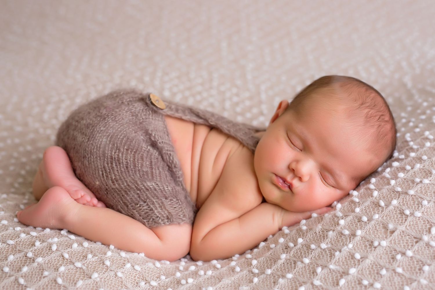 Sleeping newborn wearing gray knit pants on textured white blanket. San Diego Newborn Photographer