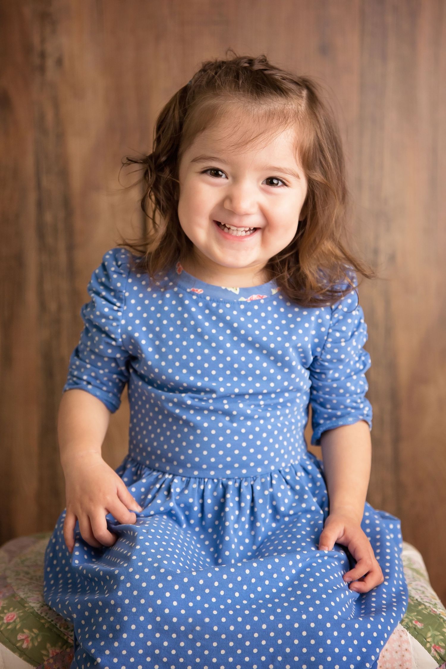 San Diego Family photographer captures A child wearing a blue polka dot dress smiles during an indoor portrait session in San Diego .