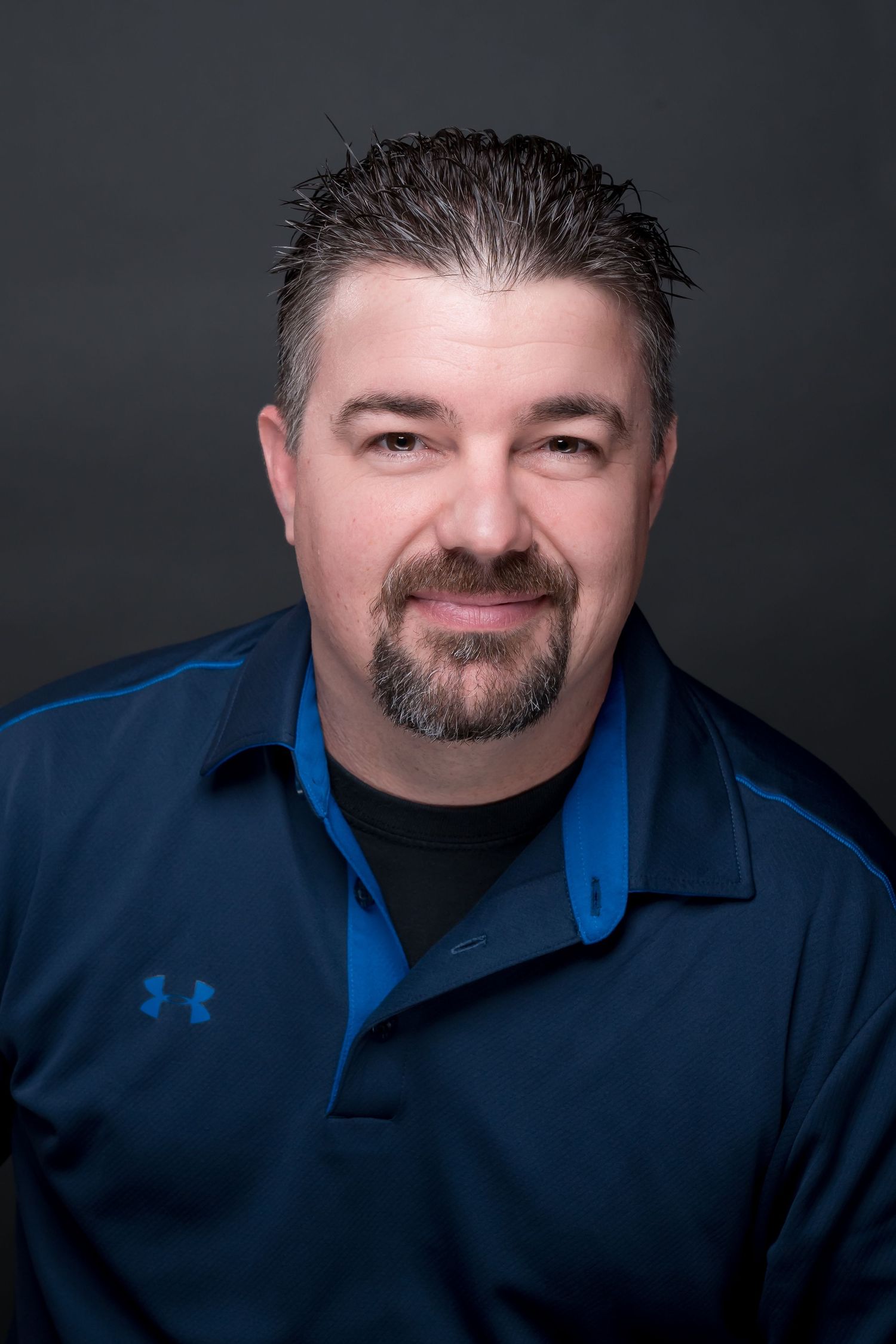 Professional headshot of man in blue dress shirt against dark background