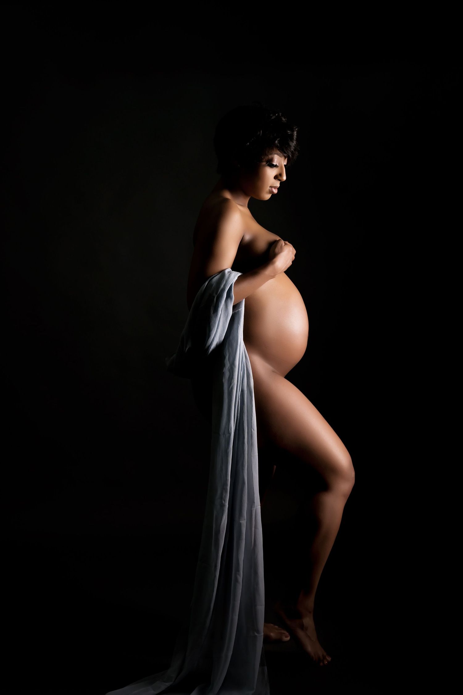 Artistic silhouette maternity photo with draped fabric against dark background.