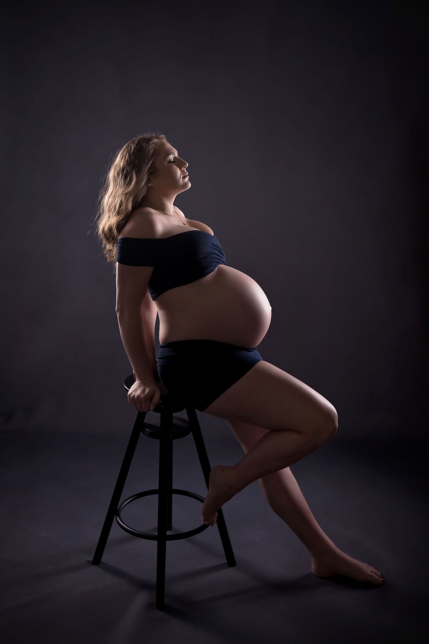 Maternity silhouette seated on a chair against a dark studio background